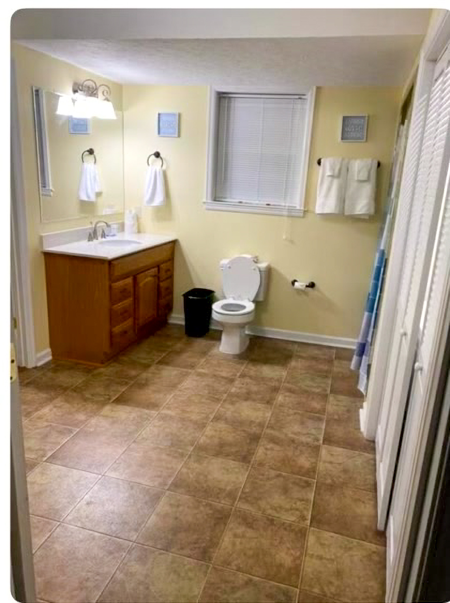 Spacious bathroom with a single-sink vanity on the left, a toilet beneath a window, towel racks on the wall, and tan tile flooring inside the home of Sponsored Residential Providers Takeyshia Gibson and Antonio Carter in Forest, Virginia.