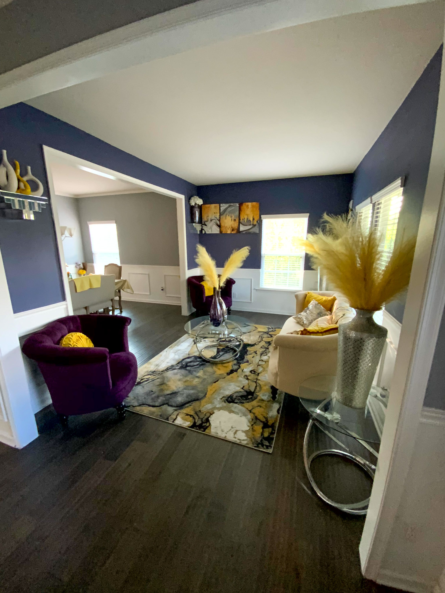 A modern sitting room features purple and white chairs, a patterned rug, and decorative yellow accents arranged throughout the space inside the home of Sponsored Residential Provider Derrick Moseley in Richmond, Virginia.