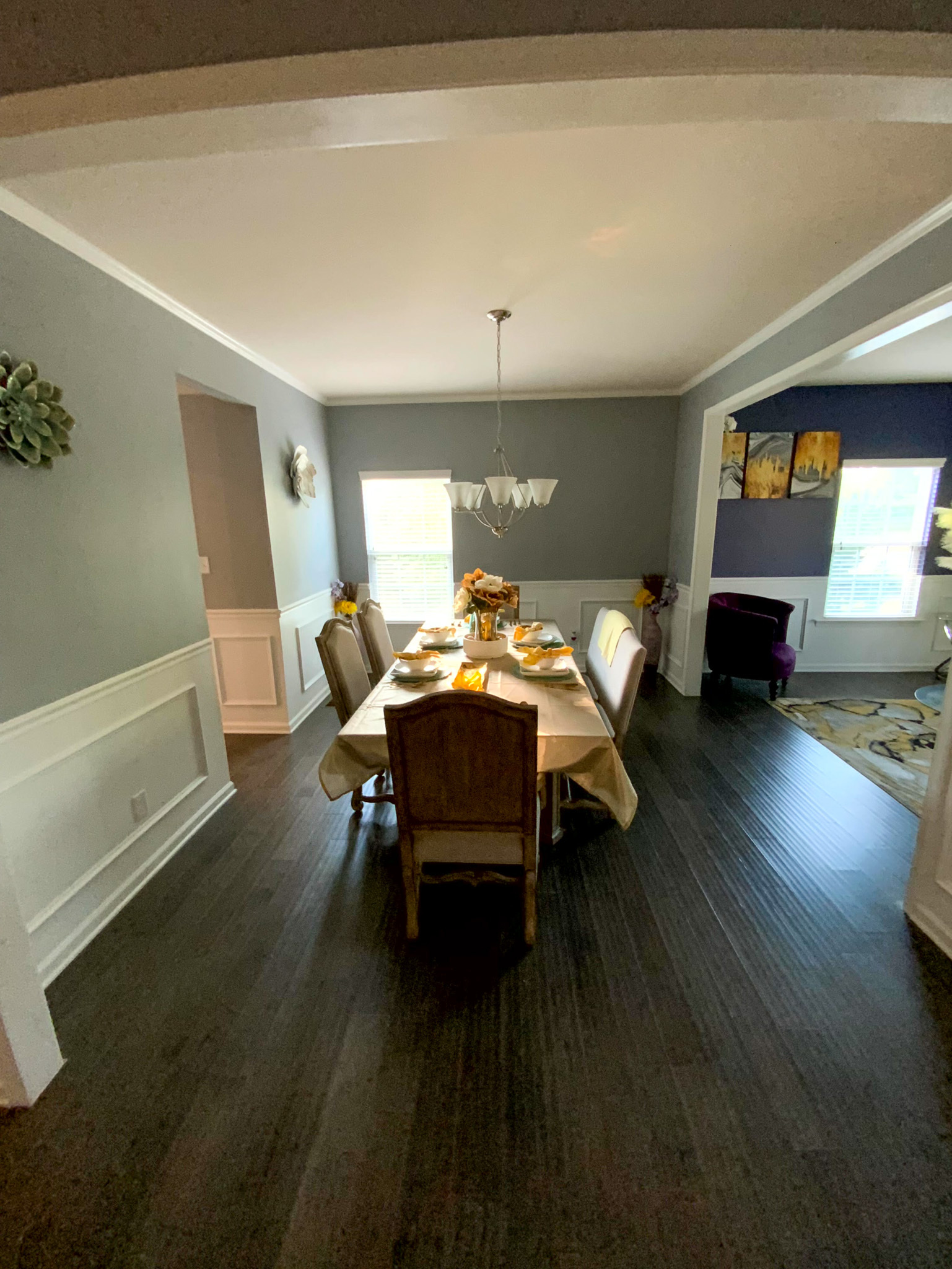 A dining room features a set table with six chairs, dark wood floors, and decorative accents placed around the space inside the home of Sponsored Residential Provider Derrick Moseley in Richmond, Virginia.