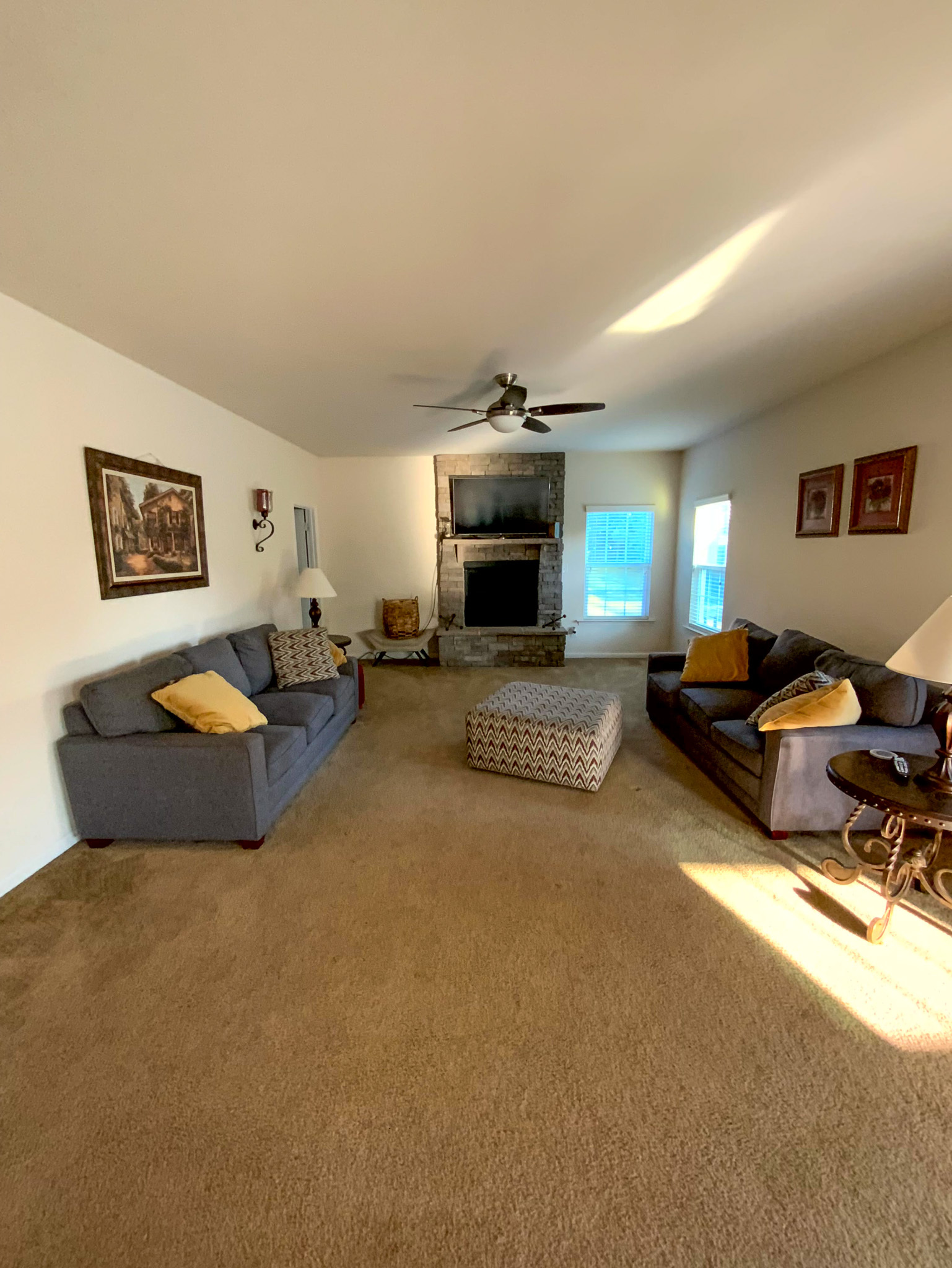A spacious living room contains two sofas, a central ottoman, and a fireplace with decor arranged around the room inside the home of Sponsored Residential Provider Derrick Moseley in Richmond, Virginia.