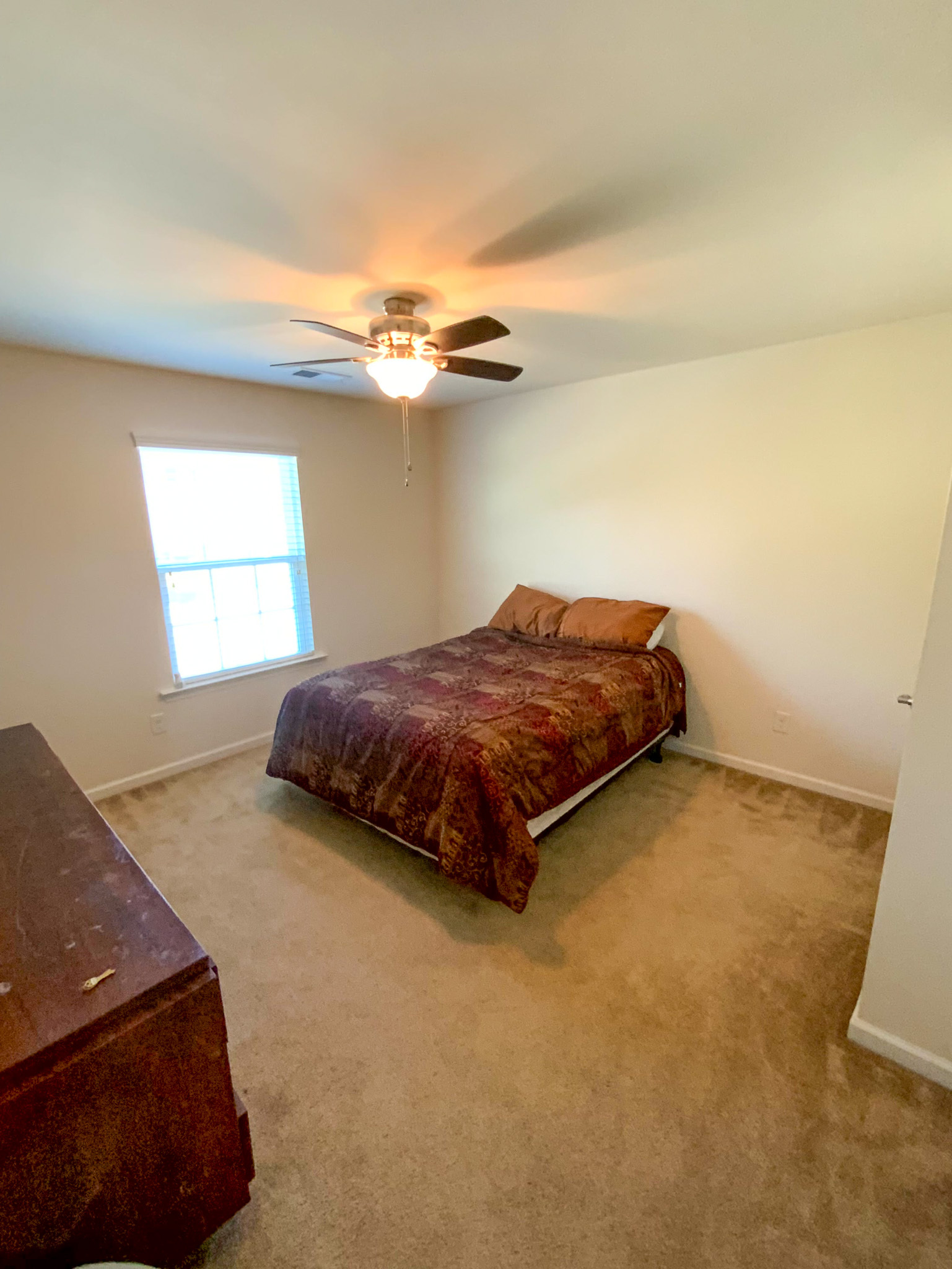 A cozy bedroom features a bed with patterned brown bedding, a dresser, and a window that adds natural light to the room inside the home of Sponsored Residential Provider Derrick Moseley in Richmond, Virginia.