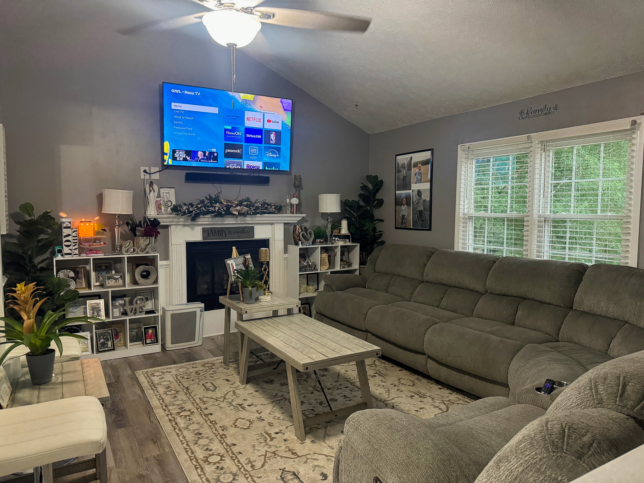 Cozy living room with gray sofas, a wall‑mounted TV above a decorated fireplace, bookshelves on both sides, and large windows letting in natural light inside the home of Sponsored Residential Providers Anthony Barnes and Demita Taylor in Forest, Virginia.