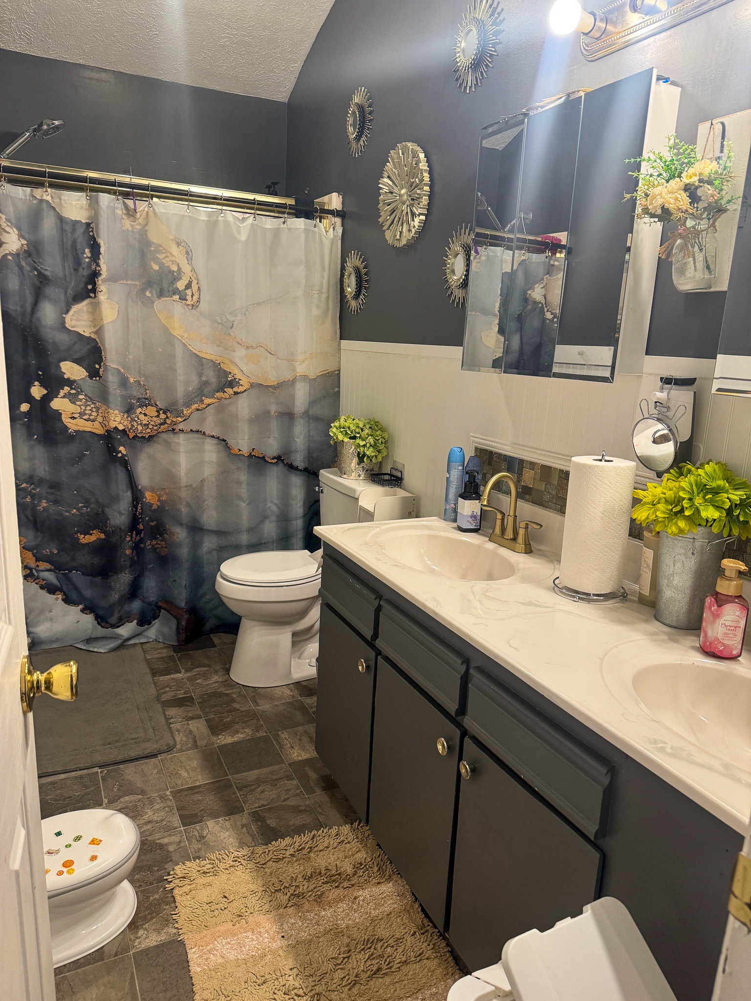 Bathroom with dark cabinets, a long white countertop, decorative mirrors, plants, and a blue‑and‑gold abstract shower curtain inside the home of Sponsored Residential Providers Anthony Barnes and Demita Taylor in Forest, Virginia.