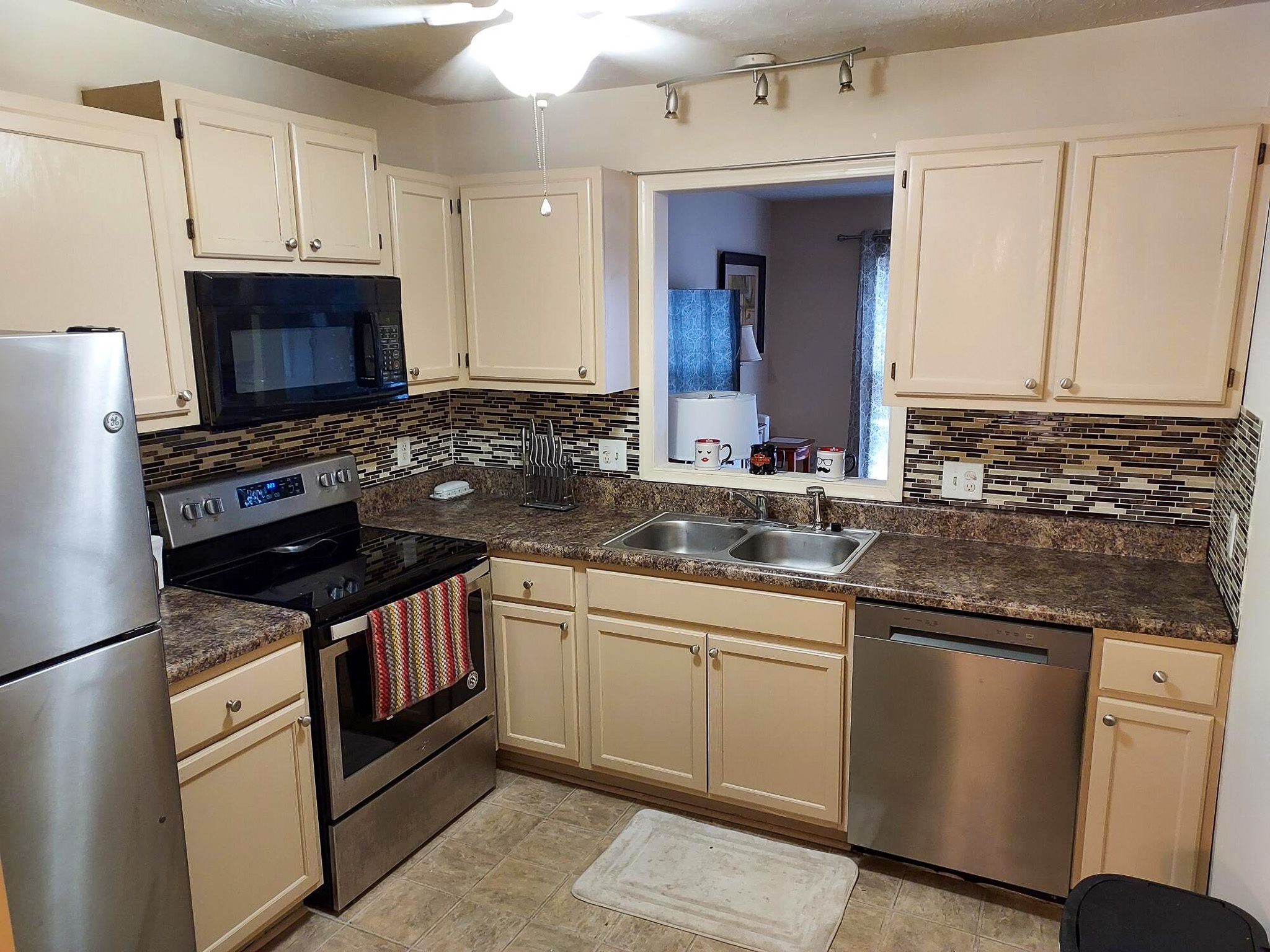 Kitchen with light cabinets, stainless steel appliances, a double sink, and patterned tile backsplash inside the home of Sponsored Residential Provider David Wilcox in Harrisonburg, Virginia.