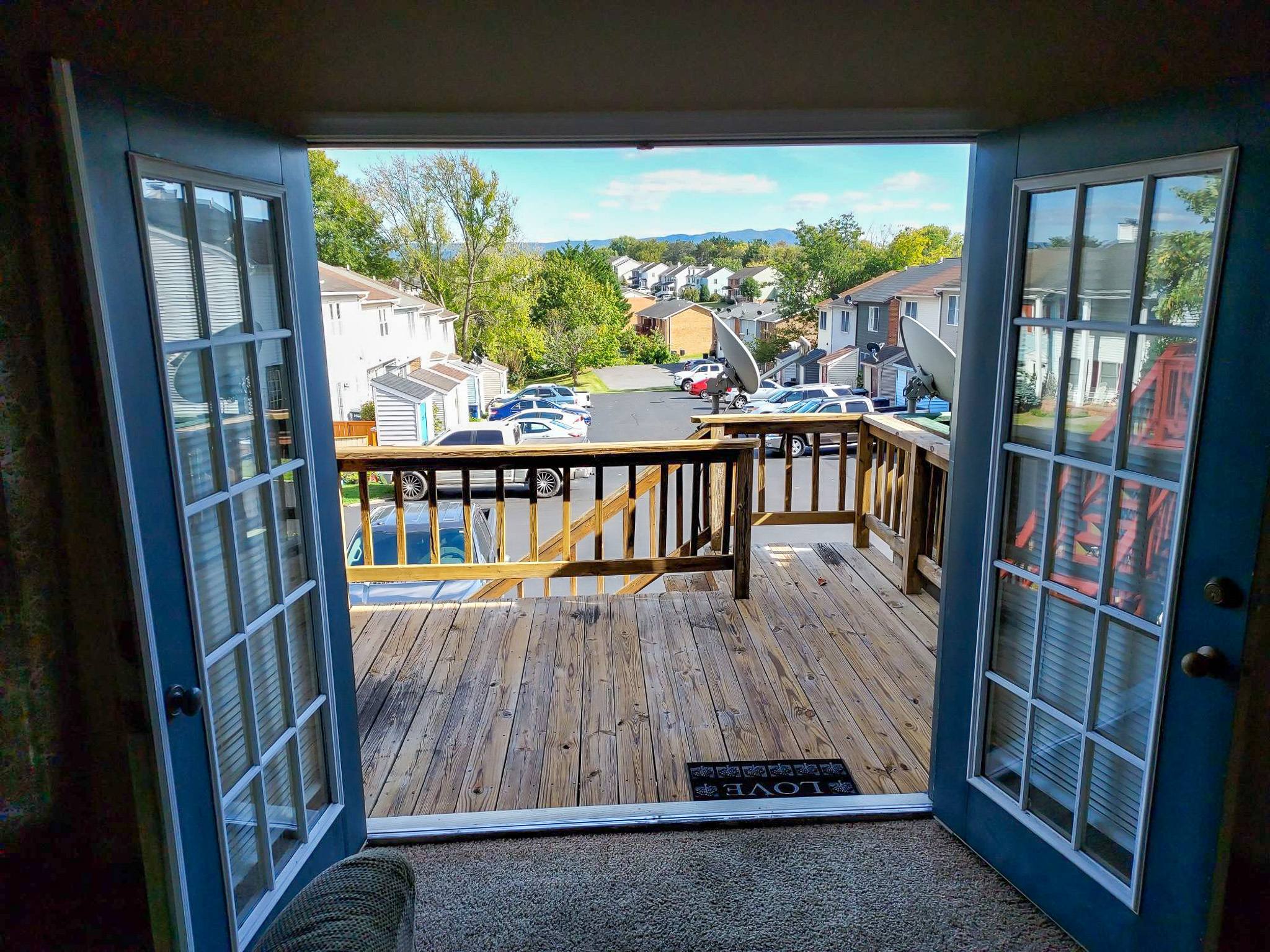 View from inside toward an open set of French doors leading to a wooden deck overlooking a townhouse community and parking area at the home of Sponsored Residential Provider David Wilcox in Harrisonburg, Virginia.