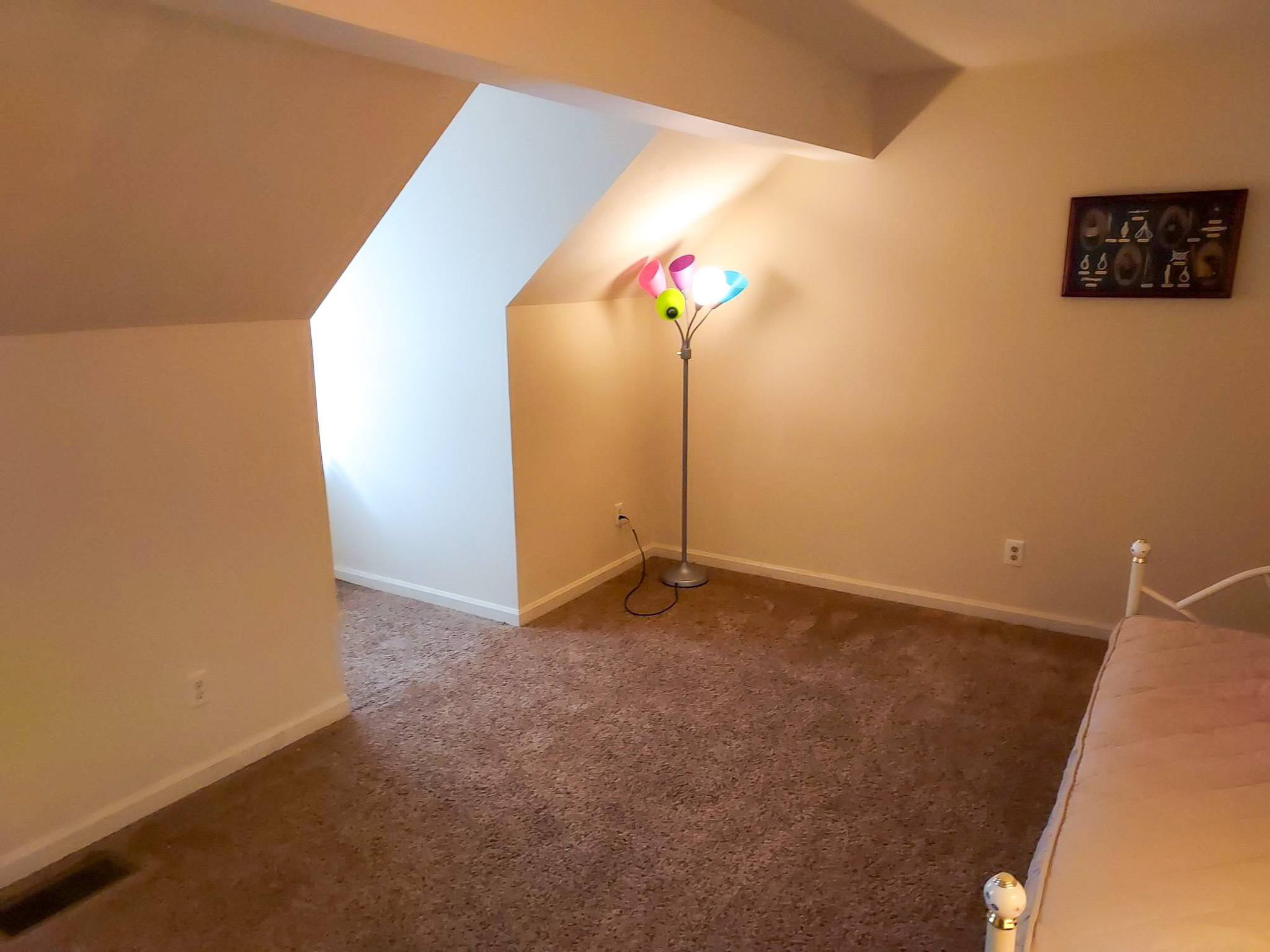 Carpeted room with sloped ceilings, a daybed on the right, and a colorful floor lamp near a recessed window alcove inside the home of Sponsored Residential Provider David Wilcox in Harrisonburg, Virginia.