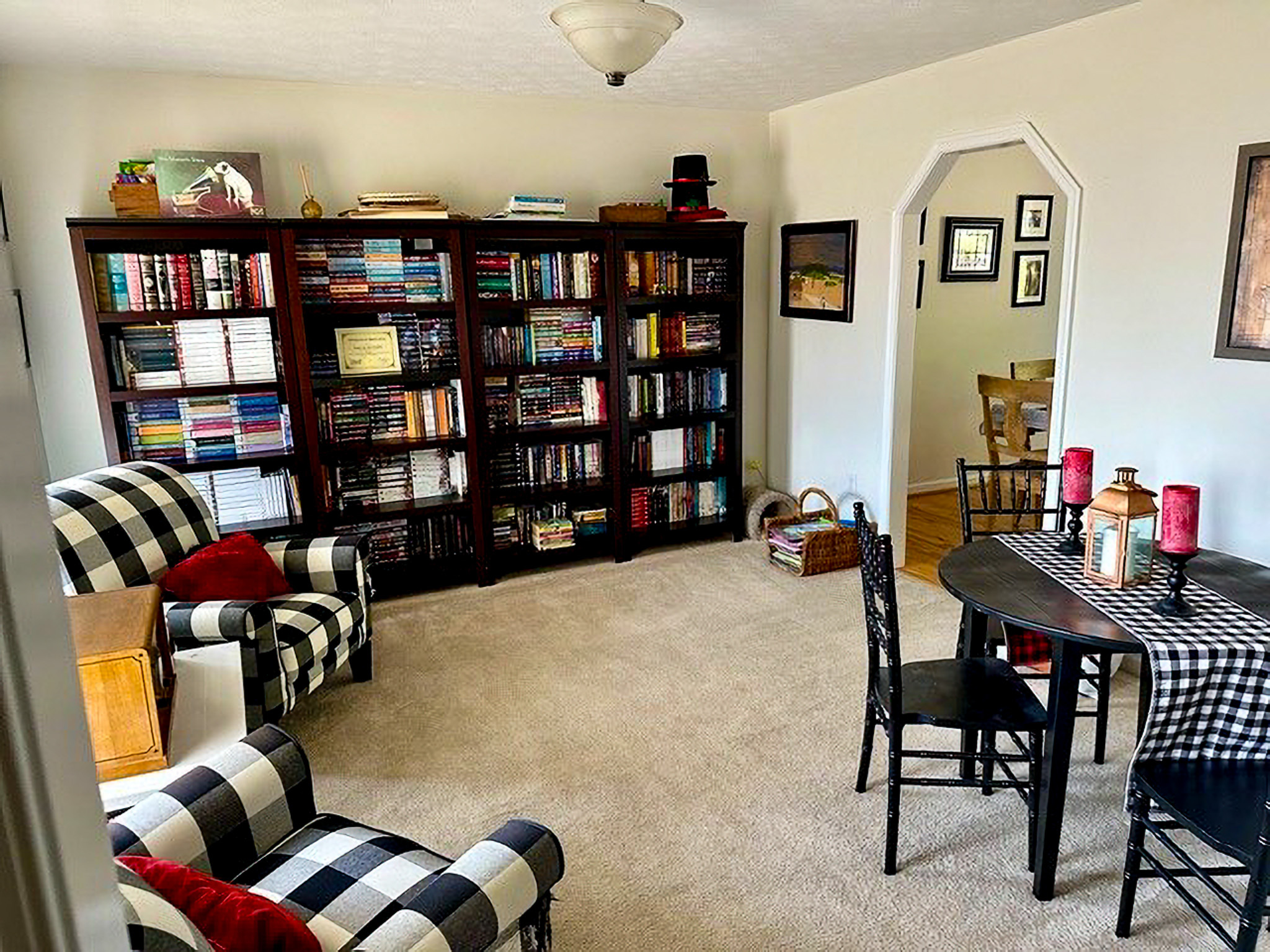 Cozy room with large bookshelves, plaid armchairs, a small round dining table, and an open doorway leading to another room inside the home of Sponsored Residential Providers Nancy and Zach Kaplan in Waynesboro, Virginia.
