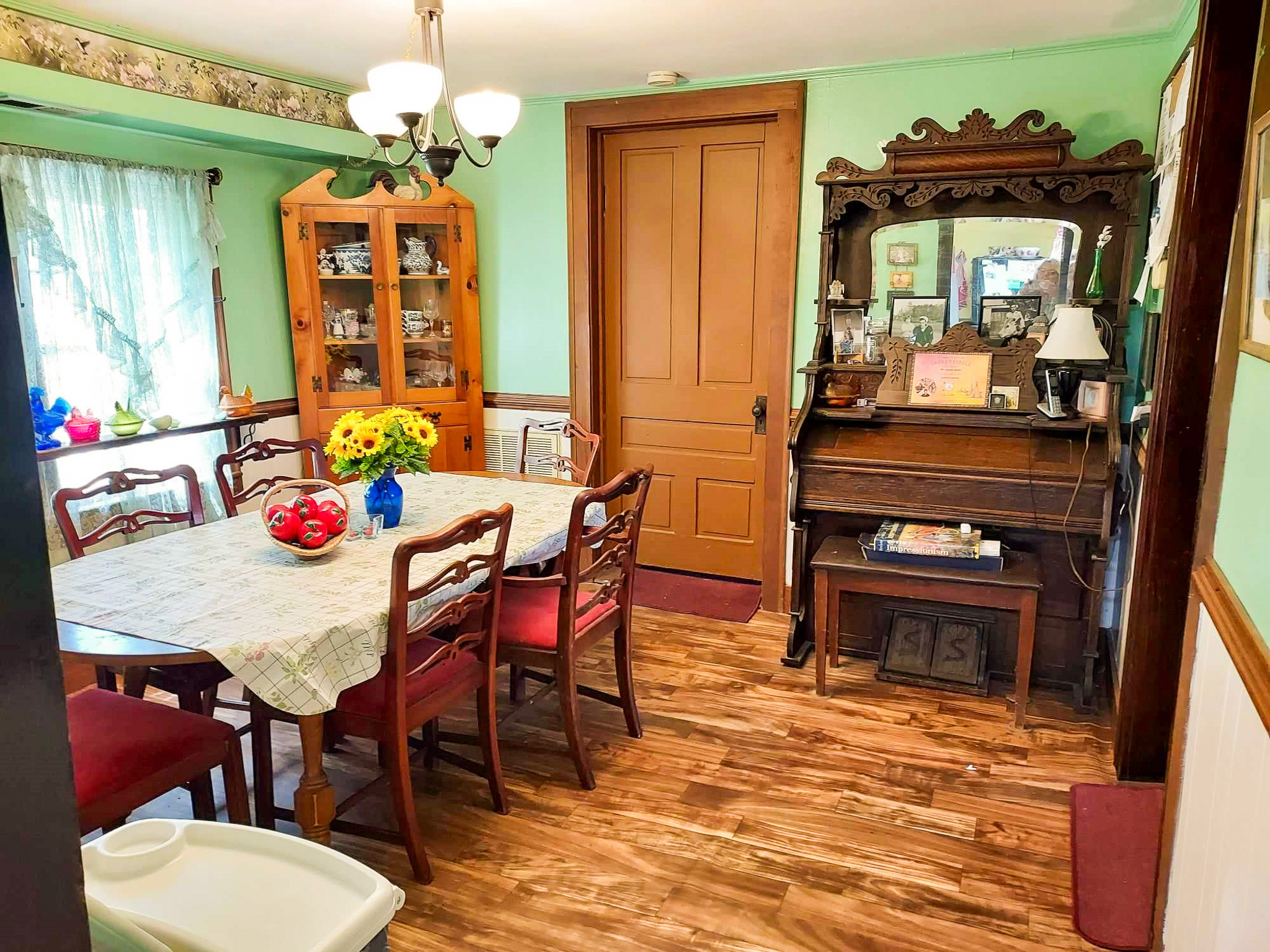 Dining room with a wooden table and red‑cushioned chairs, a china cabinet, and an ornate wooden sideboard with a mirror on mint‑green walls inside the home of Sponsored Residential Provider Angela Justice in Mathews, Virginia.