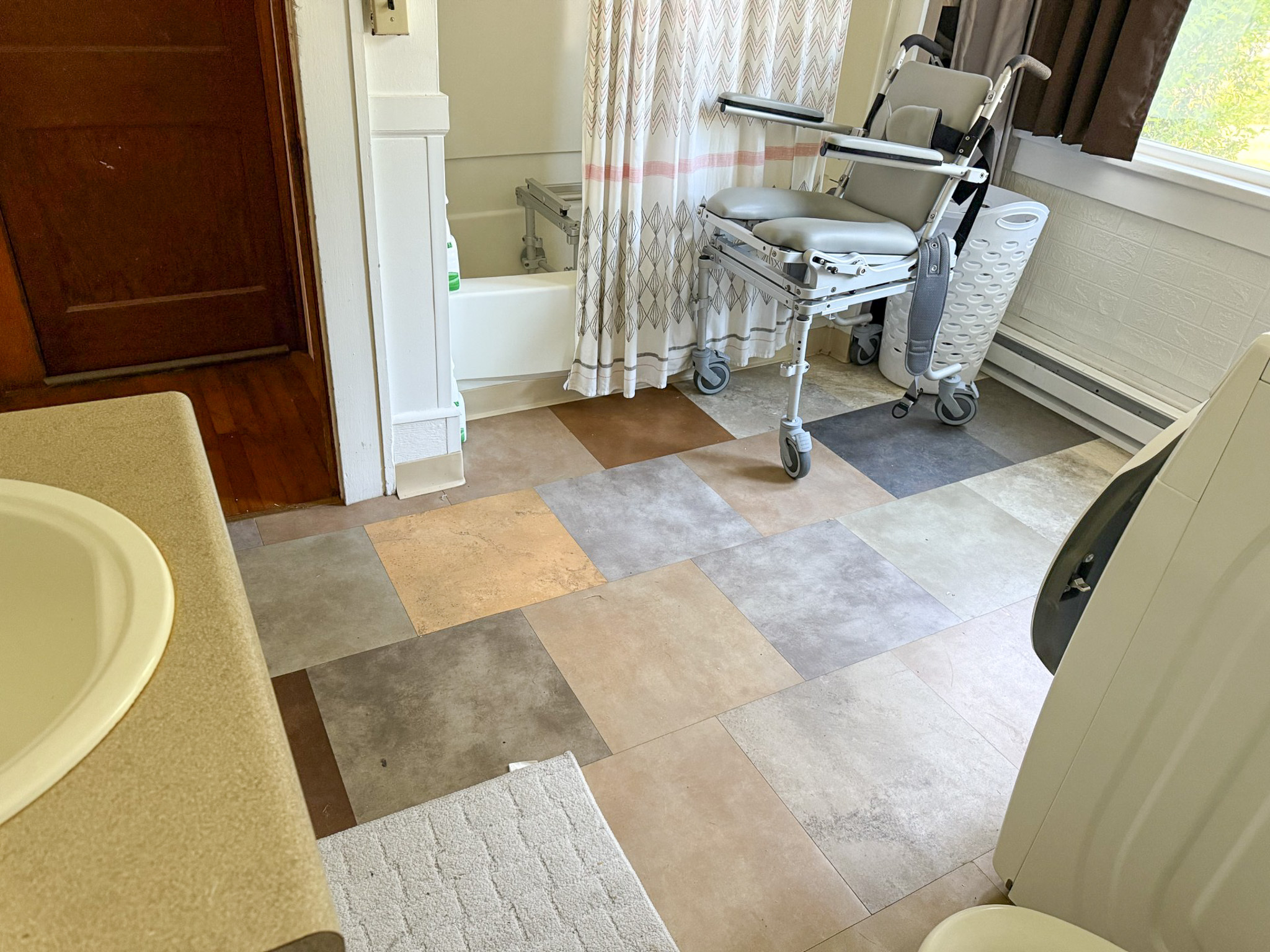Bathroom with a patterned tile floor, a shower bench next to a bathtub, and a sink countertop in the foreground inside the home of Sponsored Residential Provider Tammy Hunt in Floyd, Virginia.