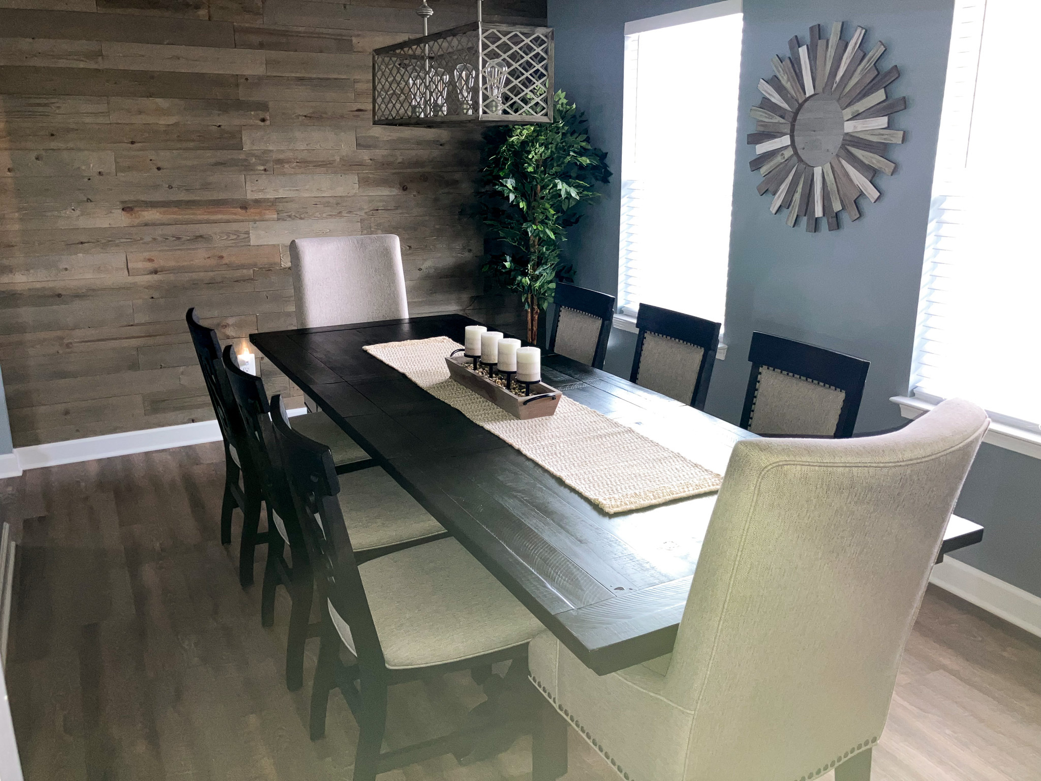 Dining room with a long dark table, cushioned chairs, wood‑accent wall, large wall clock, and a modern chandelier inside the home of Sponsored Residential Providers Crystal and Christopher Cameron in Fredericksburg, Virginia.