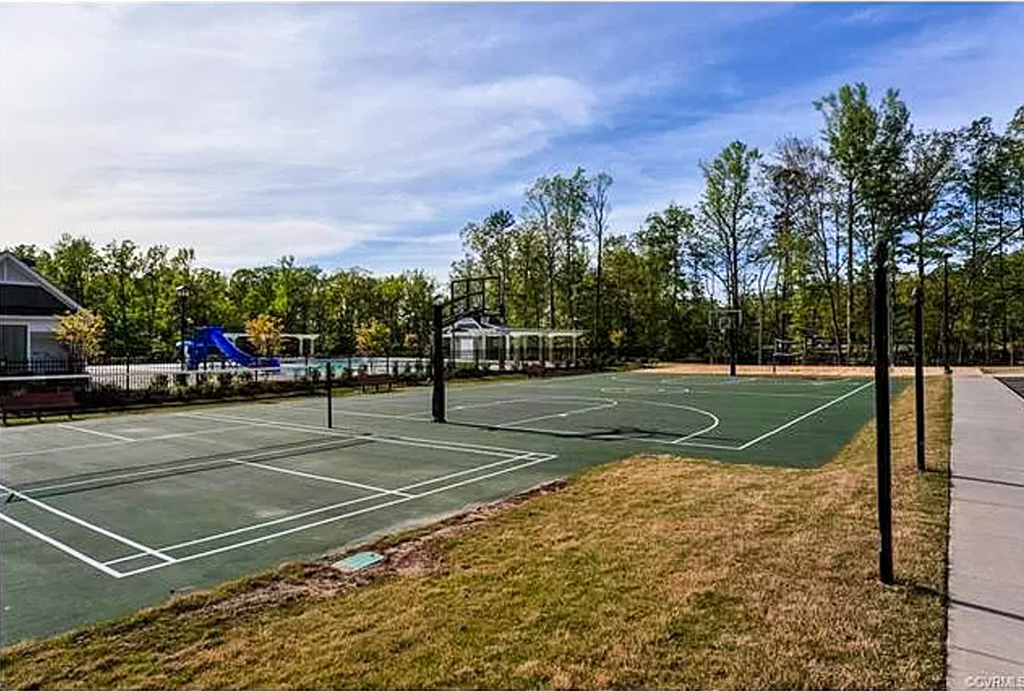 An outdoor sports area features multiple tennis and basketball courts bordered by trees in the community of Sponsored Residential Provider Derrick Moseley in Richmond, Virginia.