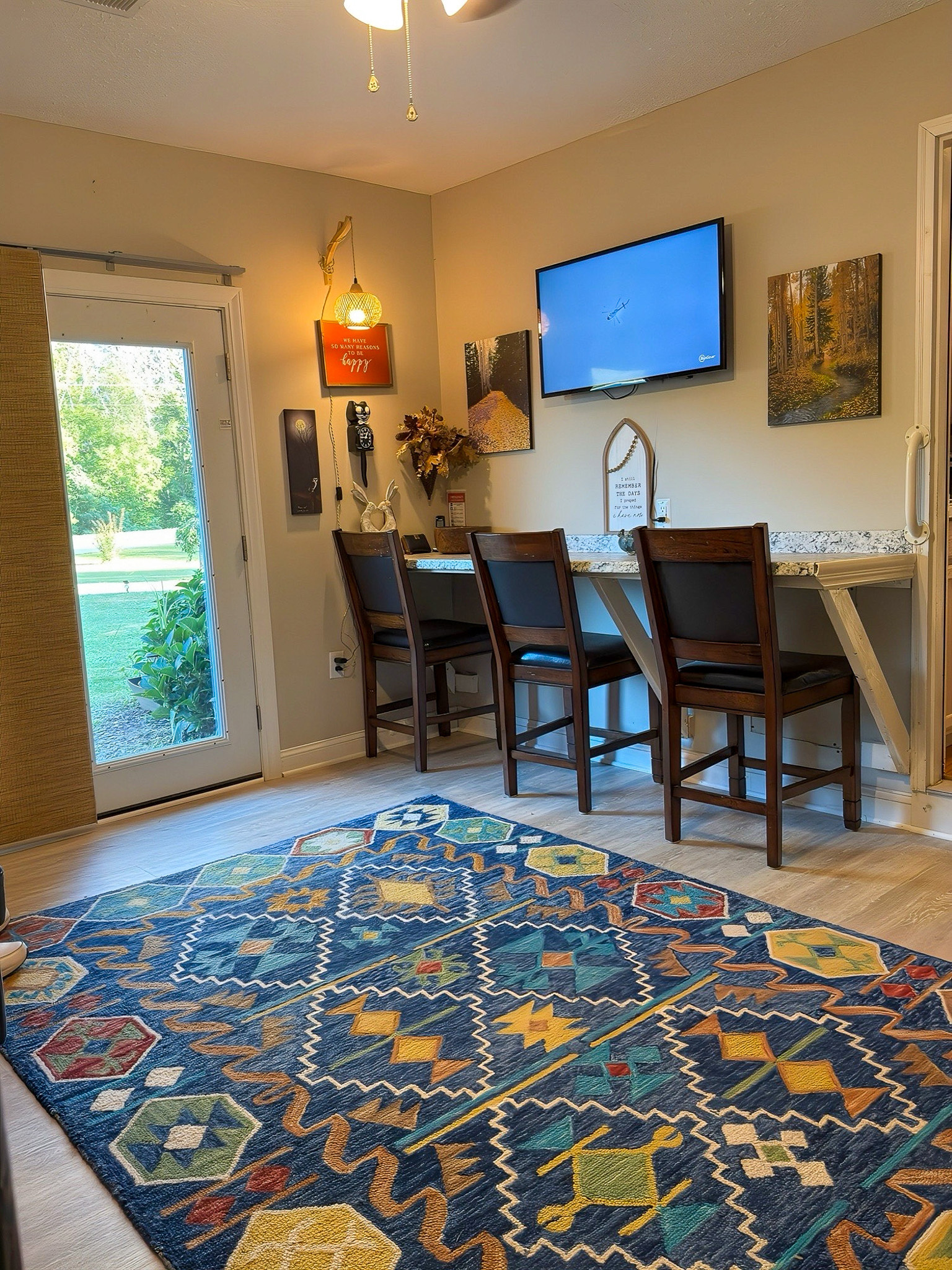 A work and craft area with a colorful patterned rug, a counter with bar stools, wall art, and a door leading outside in the home of Group Home Providers Kim and Rick Duncan in Patrick Springs, Virginia.