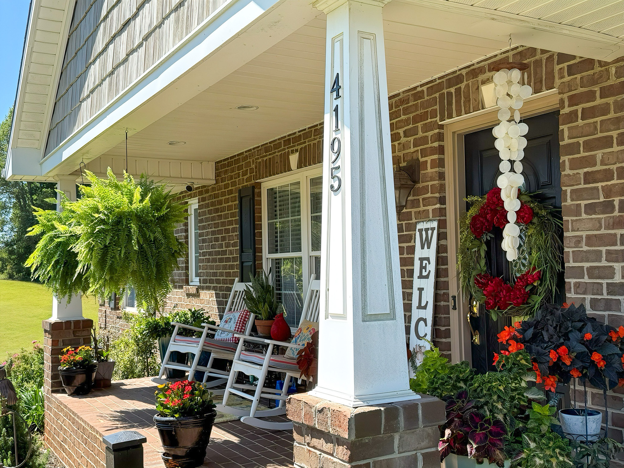 A brick front porch with rocking chairs, hanging plants, and seasonal decorations around a column marked with the house number at the home of Group Home Providers Kim and Rick Duncan in Patrick Springs, Virginia.