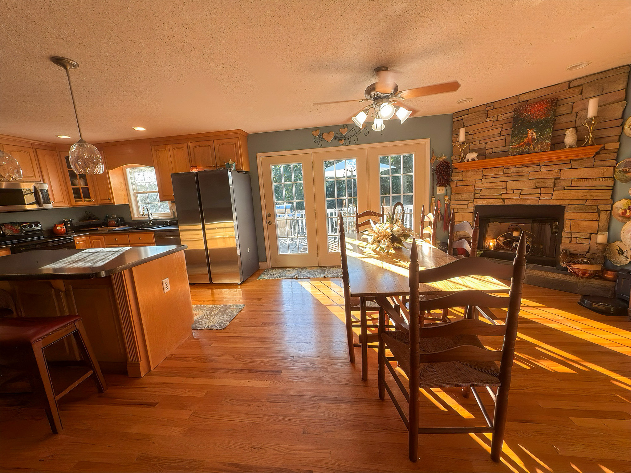 A kitchen and dining area with wood floors, wooden cabinets, a stone fireplace, and double doors leading outside inside the home of Group Home Providers Kim and Rick Duncan in Patrick Springs, Virginia.