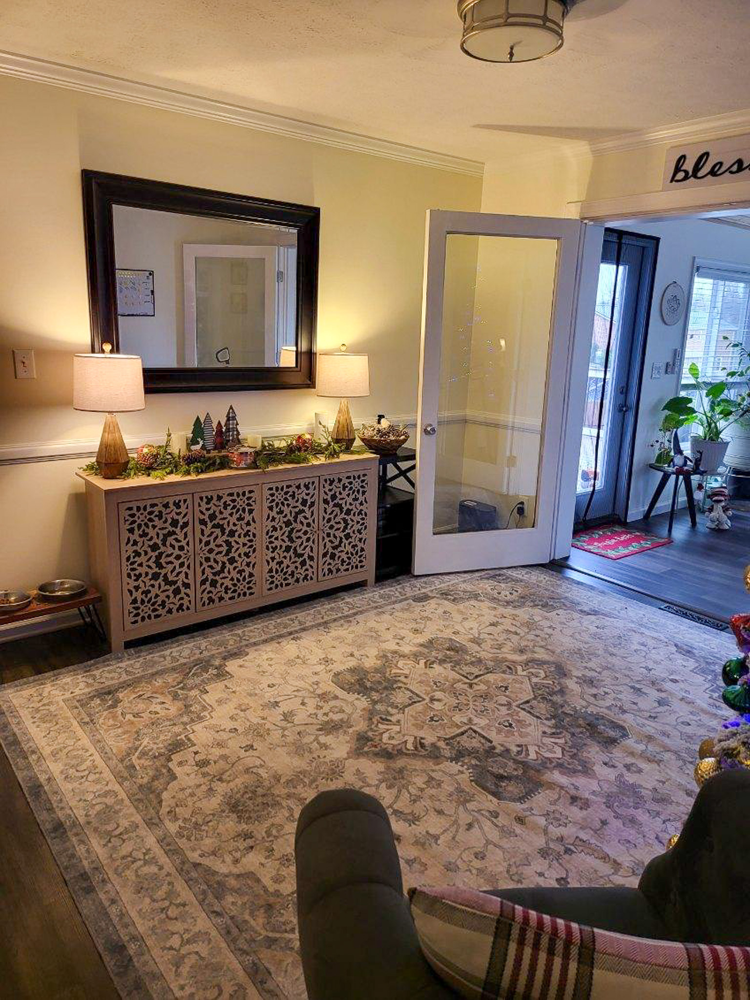 A large patterned rug sits in front of a decorative console table with lamps and a mirror beside an open glass door leading to another room  inside the home of Sponsored Residential Providers Scott and Tedra Flanders in Lynchburg, Virginia.