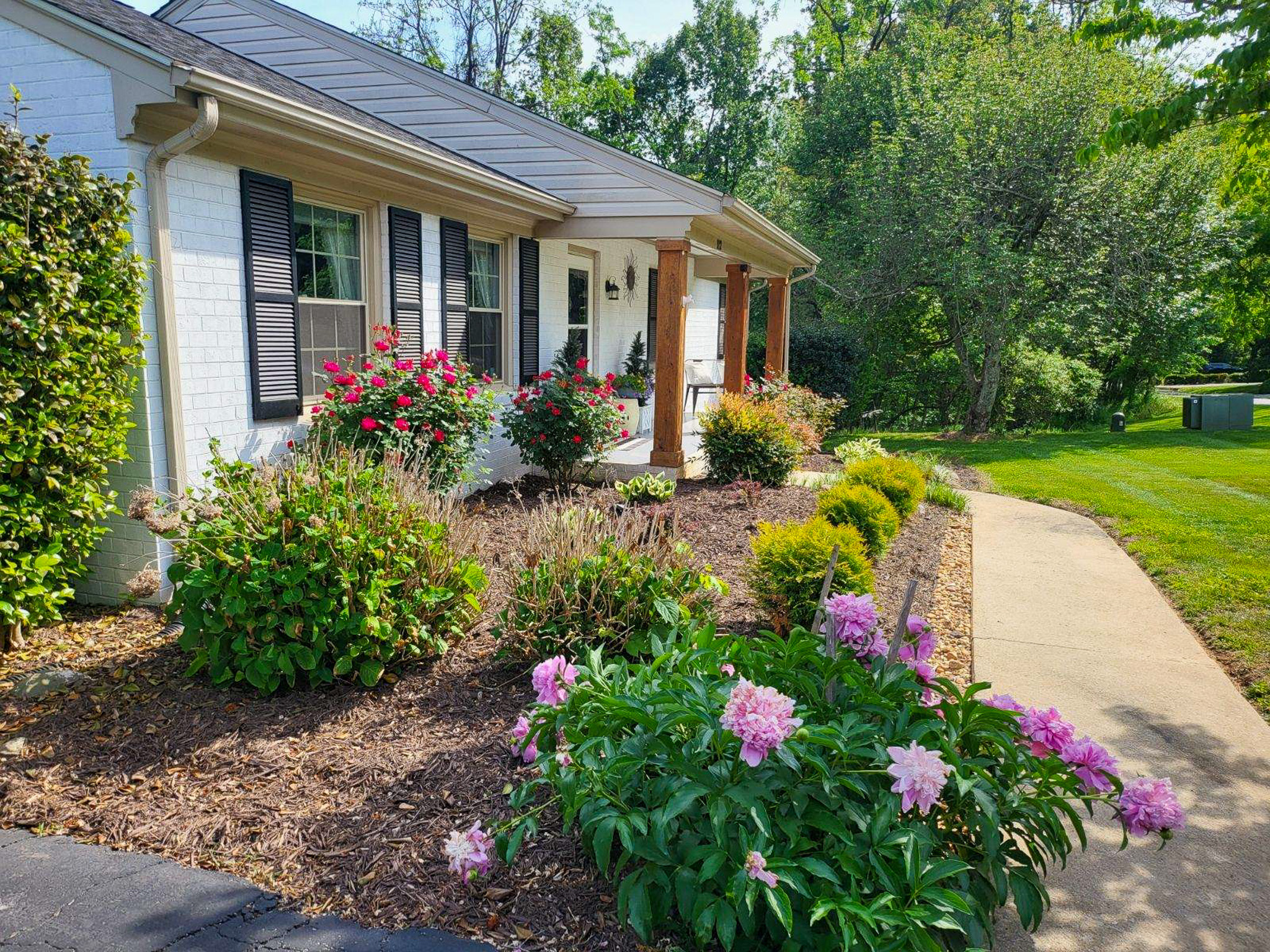 A white brick house is bordered by blooming shrubs and flowers along a mulched walkway leading toward the yard at the home of Sponsored Residential Providers Scott and Tedra Flanders in Lynchburg, Virginia.