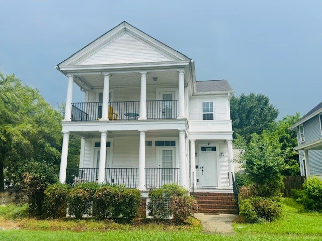 Two‑story white house with double front porches, black railings, and a small staircase, set against a cloudy sky and surrounded by shrubs belonging to Sponsored Residential Provider Greg Fortune in Norfolk, Virginia.