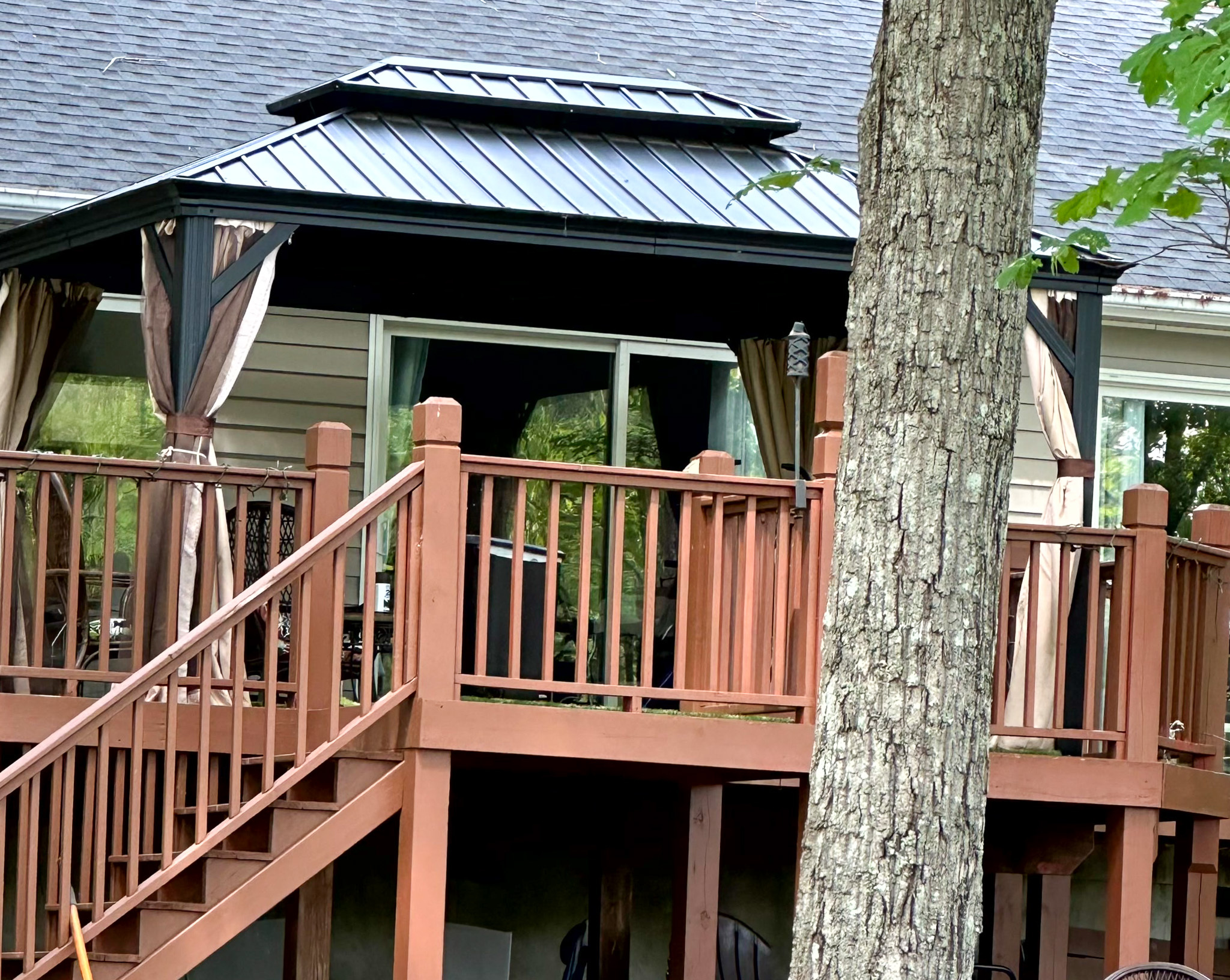 Elevated wooden deck with railings and a covered gazebo attached to a house, partially obscured by a tree outside the home of Group Home Provider Ana Garcia in Spotsylvania, Virginia.