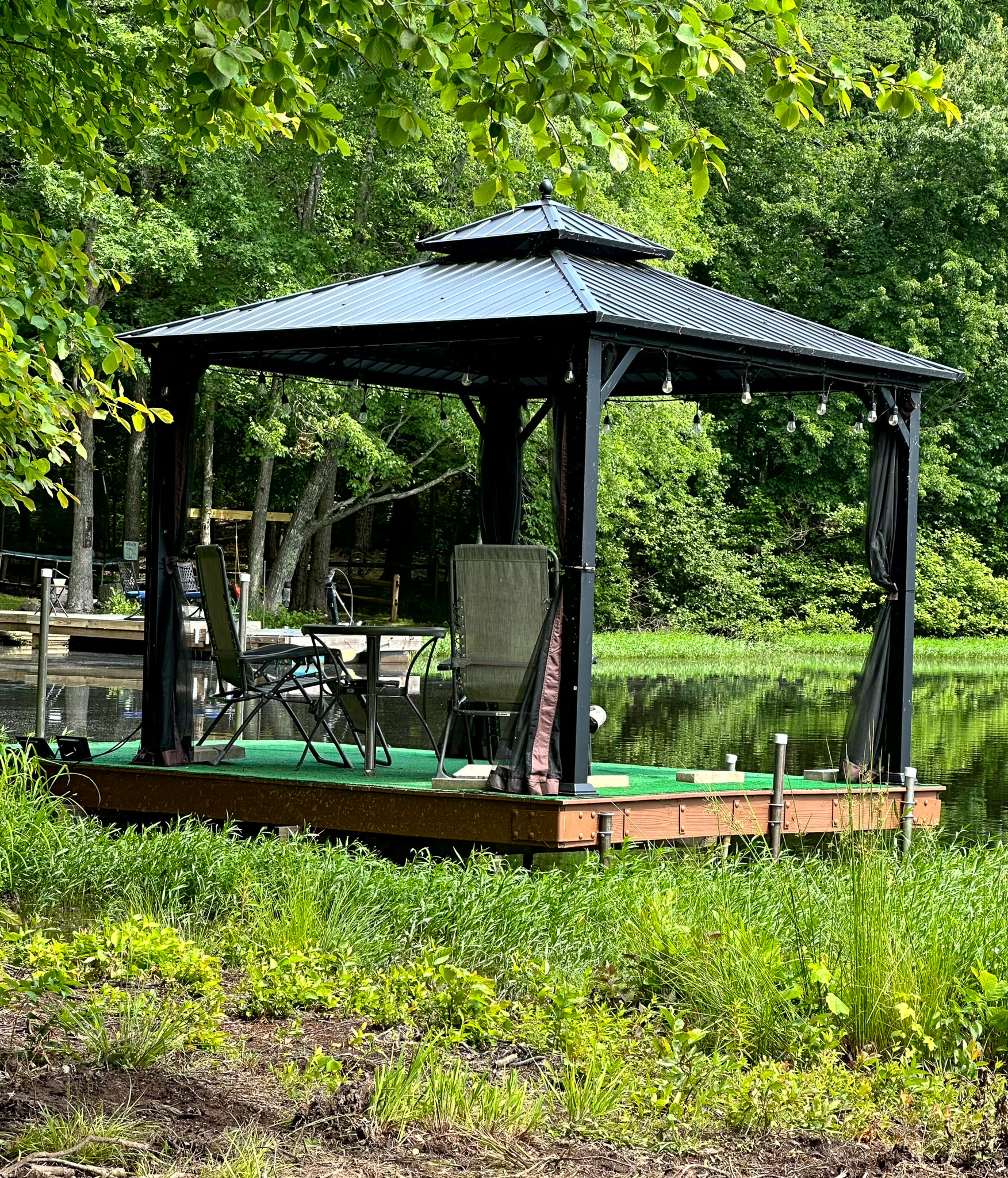 Open-sided gazebo on a wooden platform beside a calm, tree-lined lake outside the home of Group Home Provider Ana Garcia in Spotsylvania, Virginia.