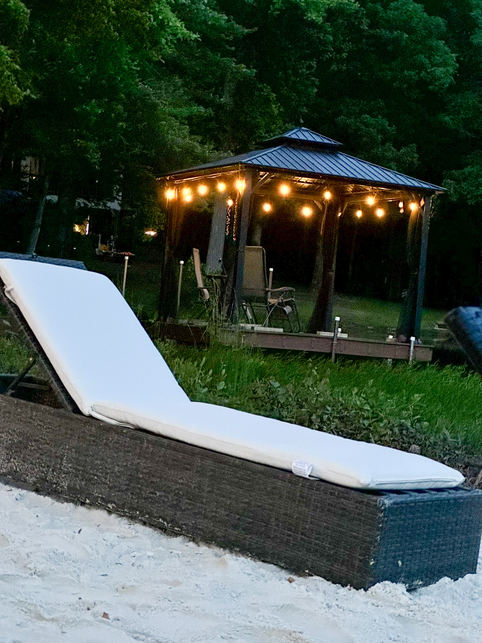 Beach lounge chair on white sand with a gazebo lit by string lights in the background at dusk outside the home of Group Home Provider Ana Garcia in Spotsylvania, Virginia.