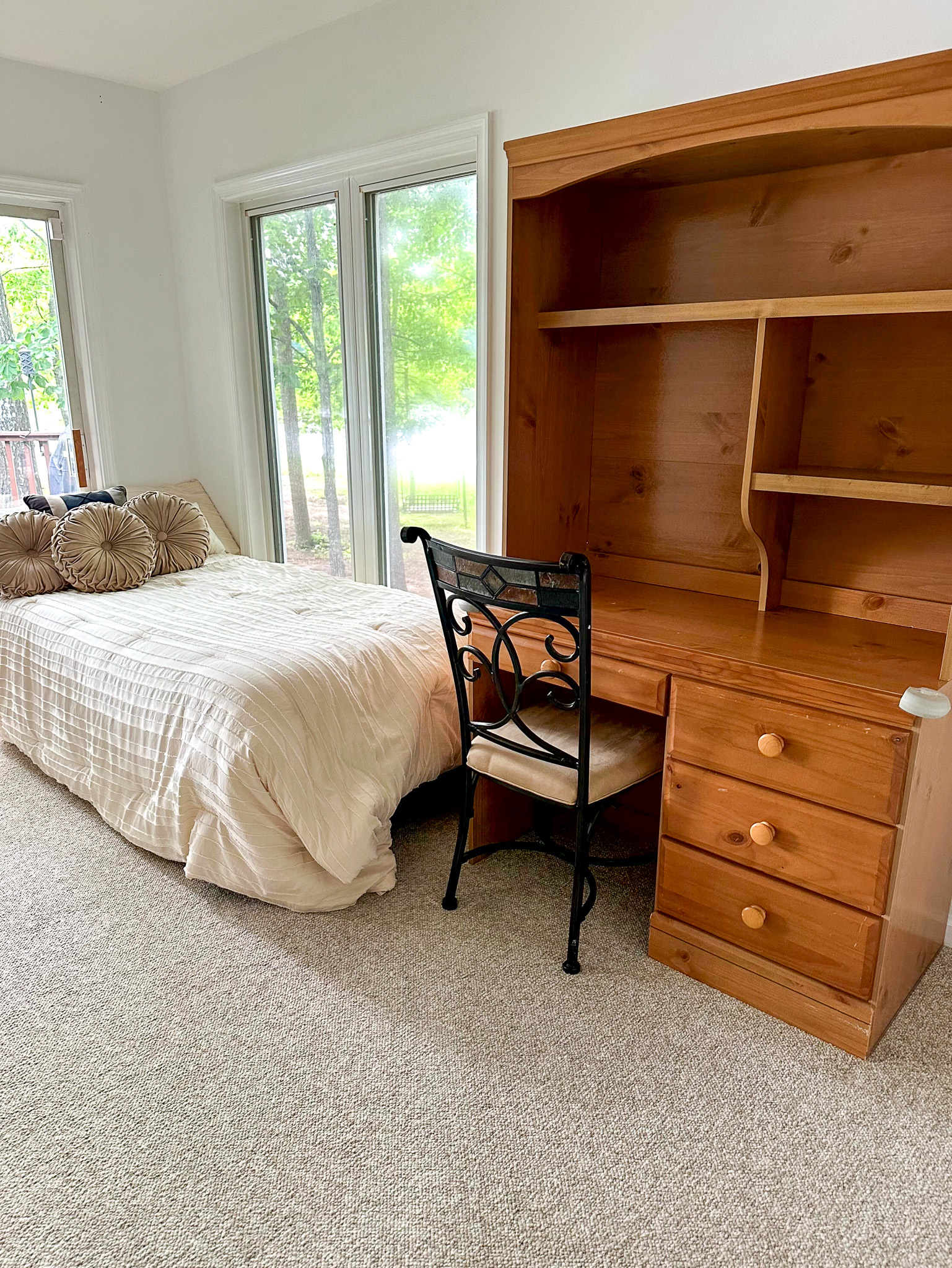 Single bed beside floor‑to‑ceiling windows with a wooden desk and chair along the opposite wall inside the home of Group Home Provider Ana Garcia in Spotsylvania, Virginia.