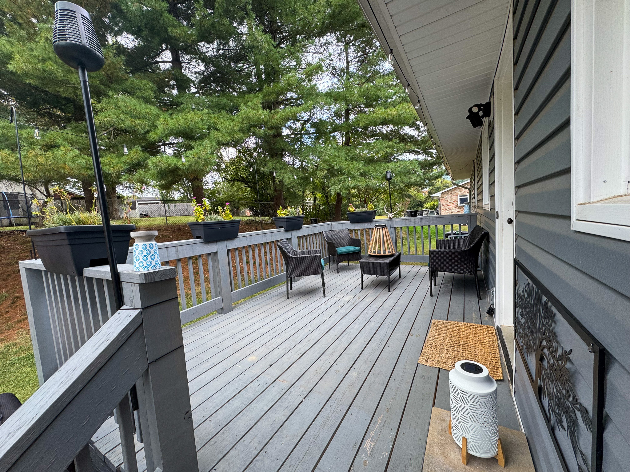 A wooden deck with outdoor chairs, planters along the railing, and a view of trees behind the house at the home of Sponsored Residential Providers Hadassah Hawks and Antonio Hernandez in Salem, Virginia.