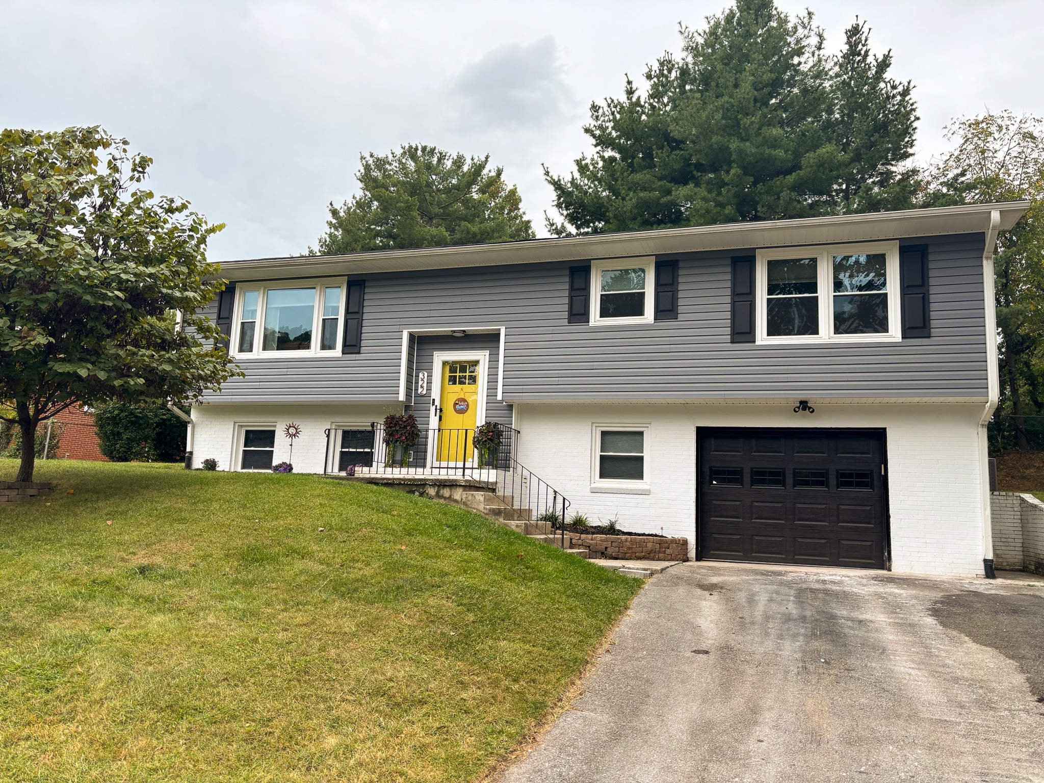 A split‑level house with gray siding, a yellow front door, black shutters, and an attached garage on a sloped lawn belonging to Sponsored Residential Providers Hadassah Hawks and Antonio Hernandez in Salem, Virginia.
