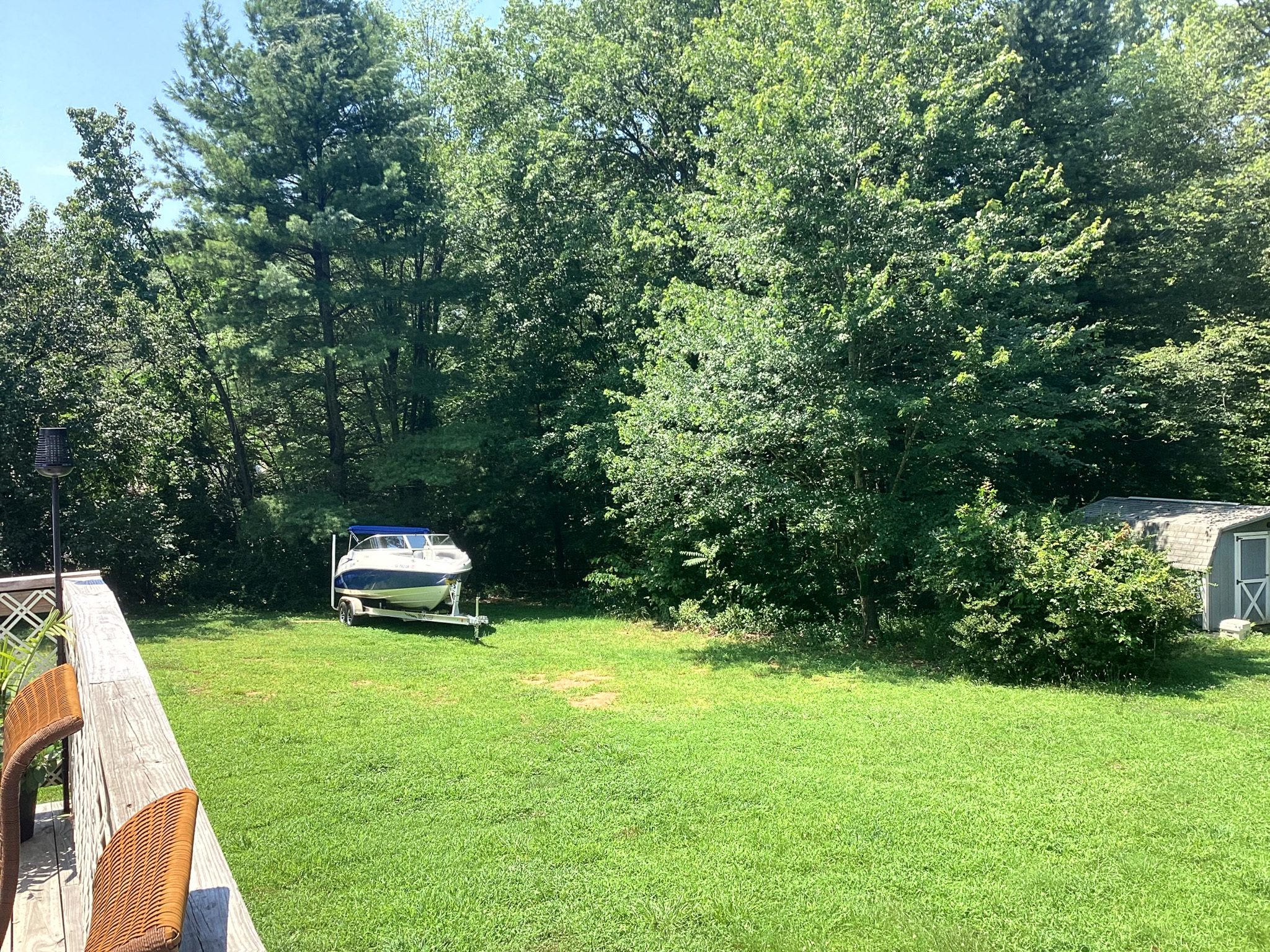 Backyard with a grassy lawn bordered by trees, a boat parked on the left, and a shed partially visible on the right at the home of Sponsored Residential Provider Kristen Hensley in Madison County, Virginia.