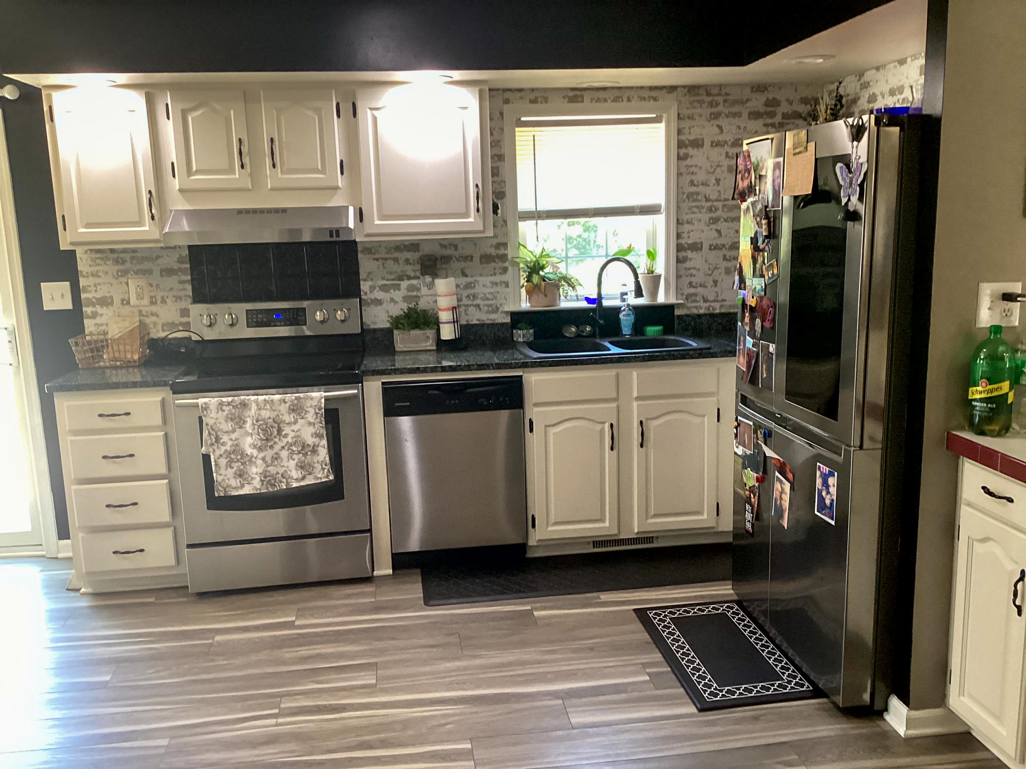 Kitchen with white cabinets, stainless steel appliances, tiled backsplash, and a window above a black countertop sink inside the home of Sponsored Residential Provider Kristen Hensley in Madison County, Virginia.