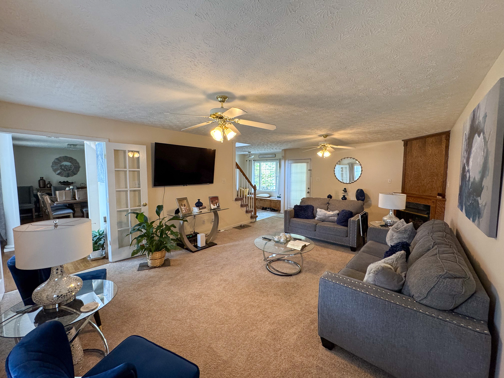 A spacious living room features gray and blue seating, a wall‑mounted TV, a fireplace, and decorative accents arranged throughout the room inside the home of Sponsored Residential Provider Durand Holloway in Chester, Virginia.