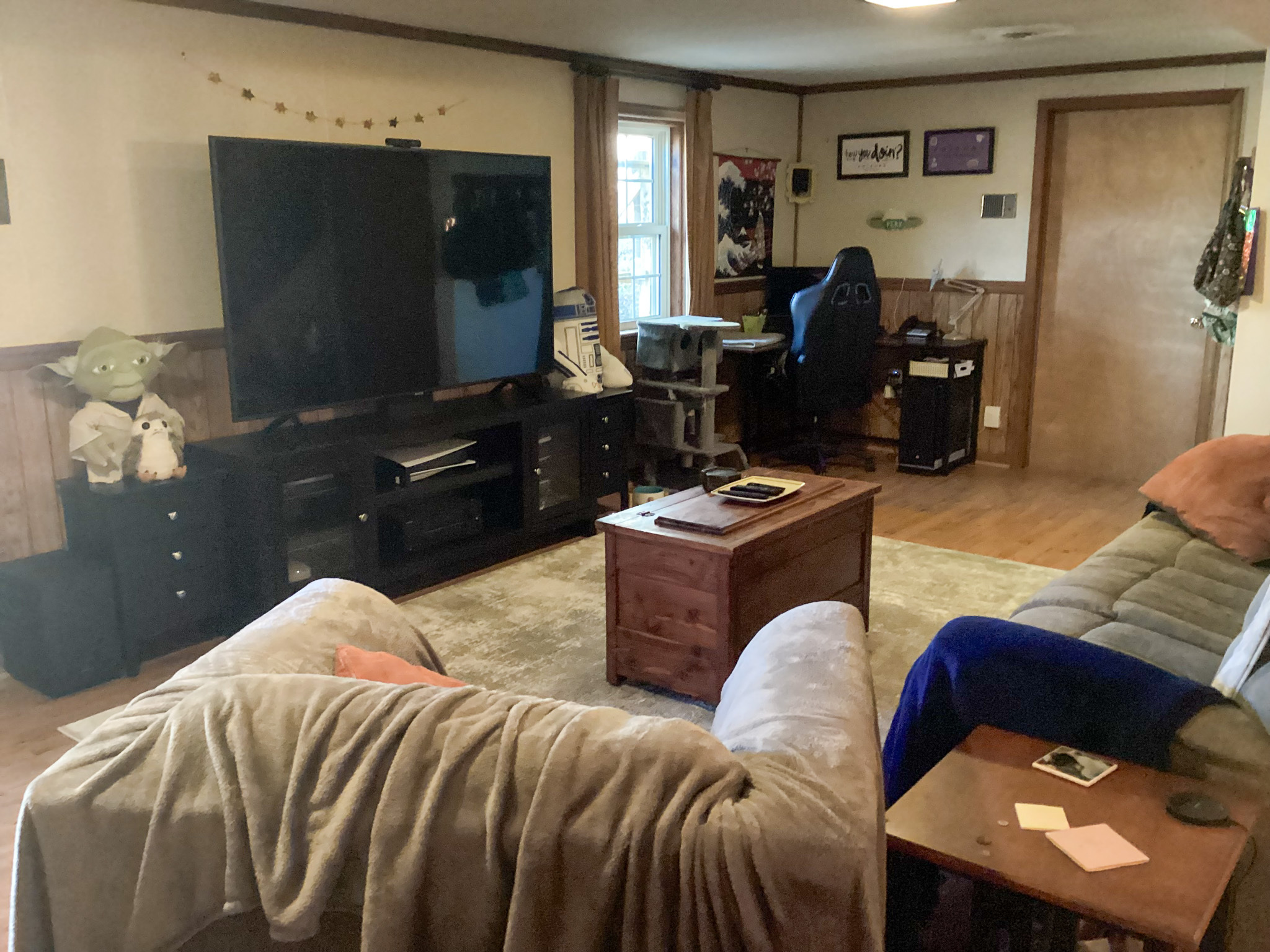 Cozy entertainment room with a large TV, two sofas, a coffee table, a gaming desk with a chair, and wood paneling along the lower walls inside the home of Sponsored Residential Providers Bill and Heather Terry in Staunton, Virginia.