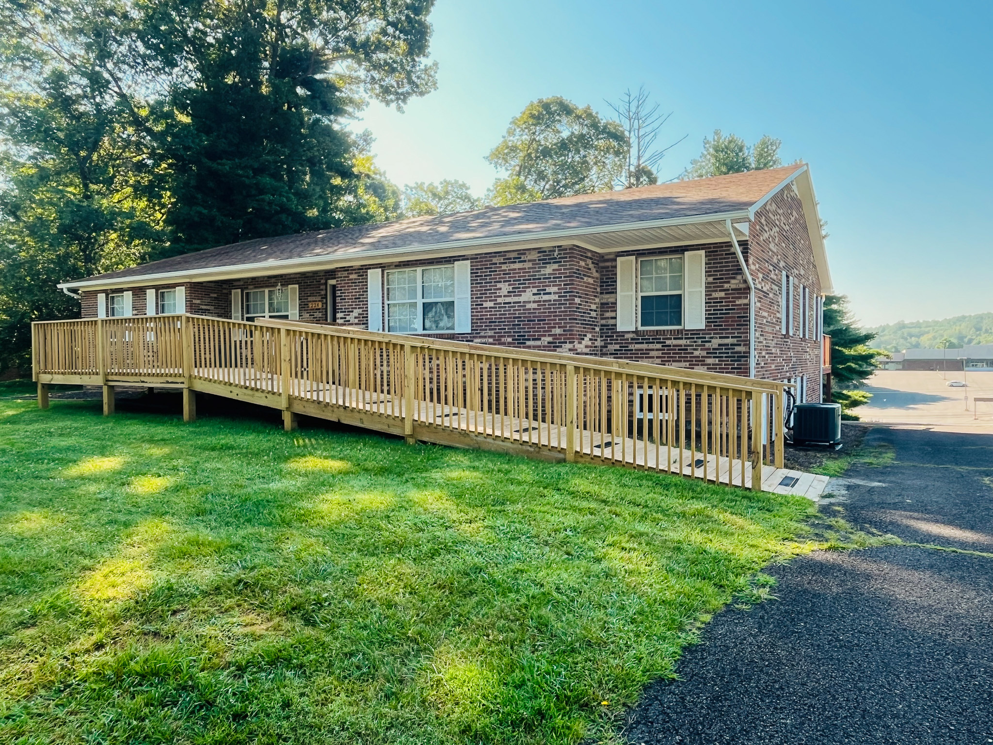 Brick house with a long wooden accessibility ramp along the front side, surrounded by green lawn and trees belonging to Sponsored Residential Providers Penny Day and Steven Coleman in Hillsville, Virginia.