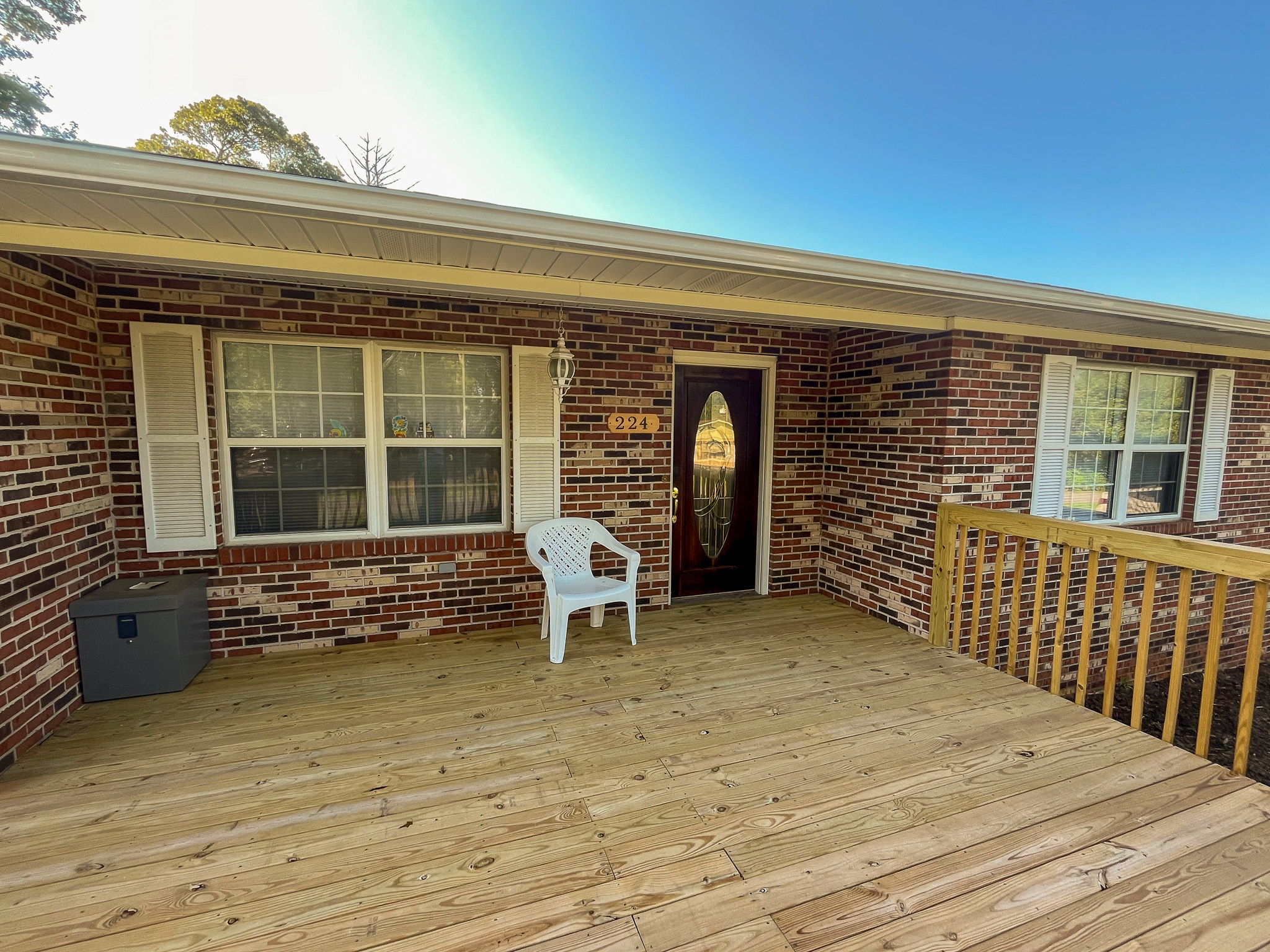 Brick house front deck with wooden flooring, white shutters, a front door with a decorative oval window, and a white plastic chair near the windows at the home of Sponsored Residential Providers Penny Day and Steven Coleman in Hillsville, Virginia.