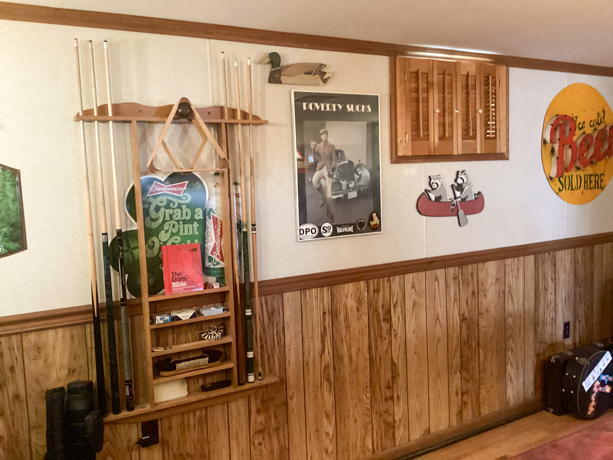 Wall with wood paneling featuring a mounted pool cue rack, various posters and decor signs, and a small shelf with accessories inside the home of Sponsored Residential Providers Bill and Heather Terry in Staunton, Virginia.