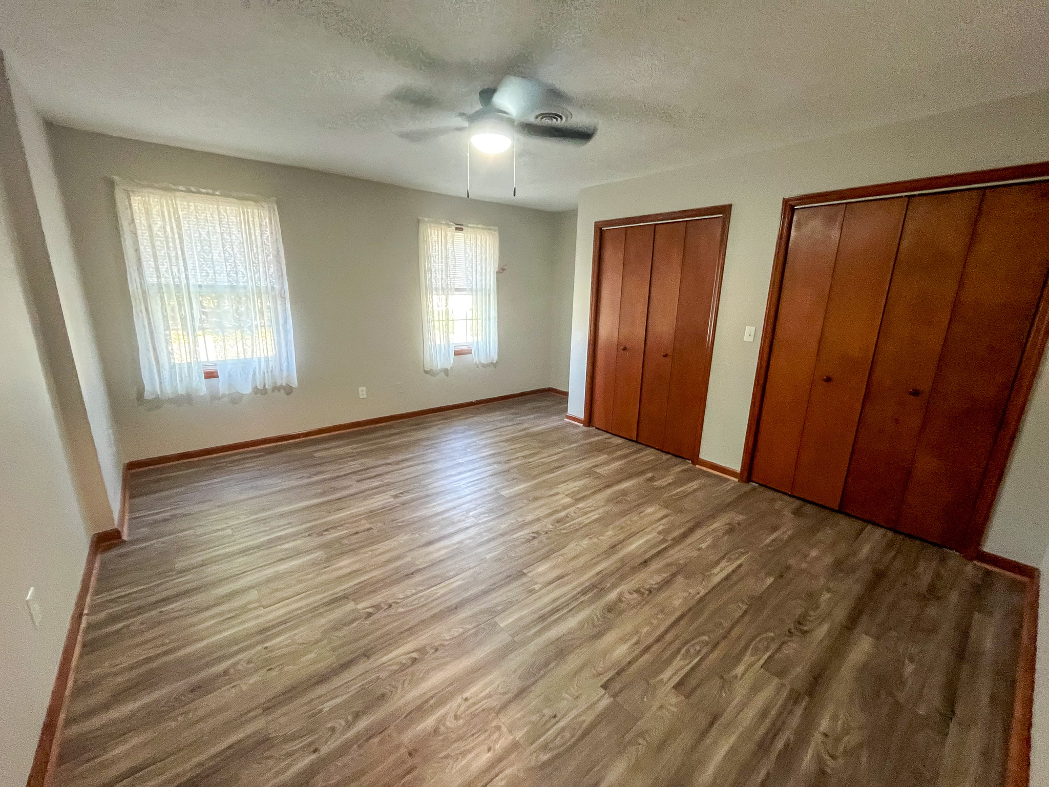 Bedroom with wood‑look flooring, two windows with sheer curtains, a ceiling fan, and two sets of wooden double-door closets  inside the home of Sponsored Residential Providers Penny Day and Steven Coleman in Hillsville, Virginia.