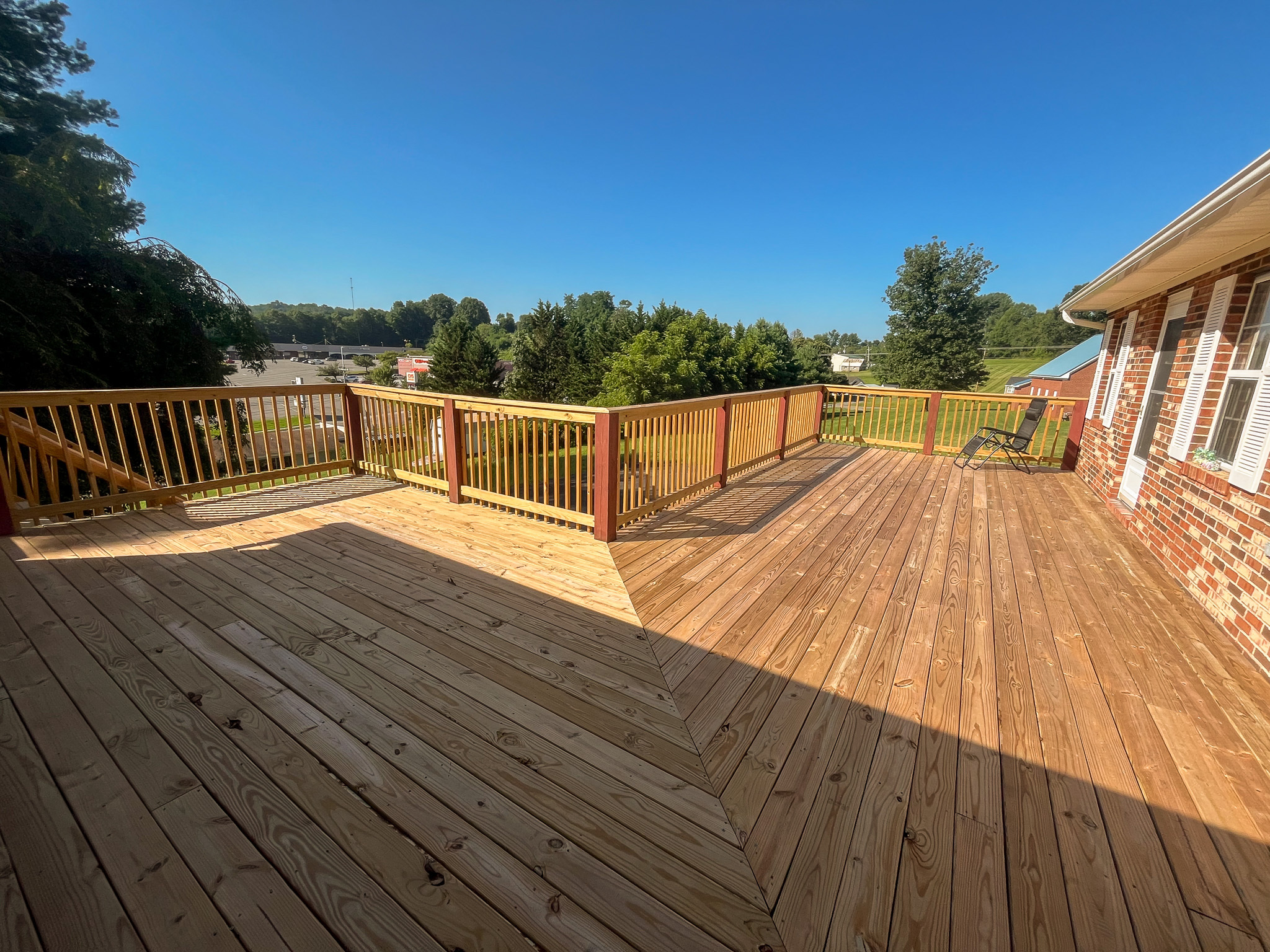 Large wooden deck with railing, extending from a brick house and overlooking a grassy yard and trees at the home of Sponsored Residential Providers Penny Day and Steven Coleman in Hillsville, Virginia.