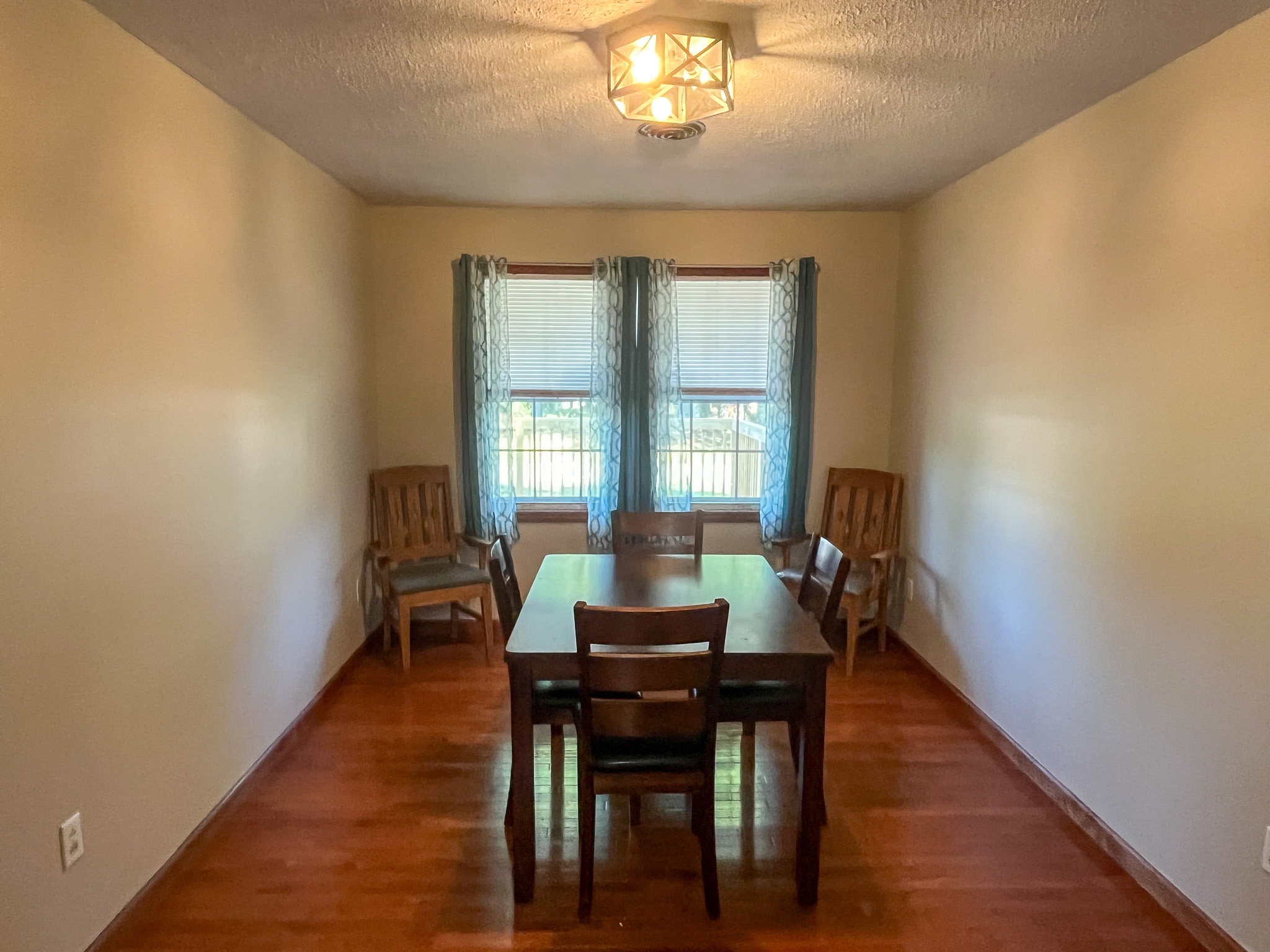 Simple dining room with hardwood floors, a small table with four chairs, two windows with blue curtains, and two additional wooden chairs against the wall inside the home of Sponsored Residential Providers Penny Day and Steven Coleman in Hillsville, Virginia.