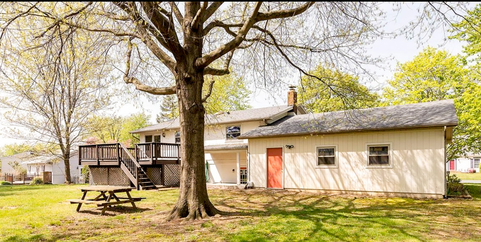 Back view of a split‑level house with a raised deck, large tree, picnic table, and attached structure with an orange door outside the home of Sponsored Residential Providers Daynesha and Karen Wilson in Stephens City, Virginia.