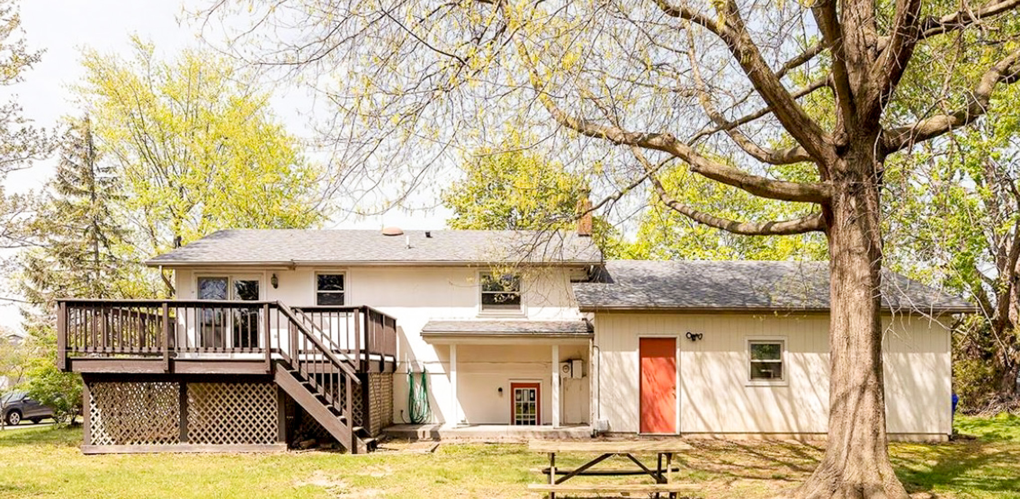 Back of a split‑level house with a wooden deck, an attached structure with an orange door, and a large tree and picnic table in the yard Sponsored Residential Providers Daynesha and Karen Wilson in Stephens City, Virginia.