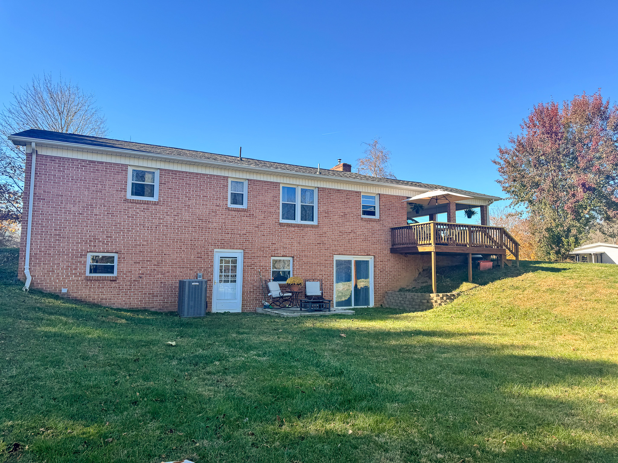 The back of a two‑story brick house with multiple windows, a raised wooden deck on the right, and a grassy sloped yard belonging to Sponsored Residential Provider Pamela Hill in Austinville, Virginia.