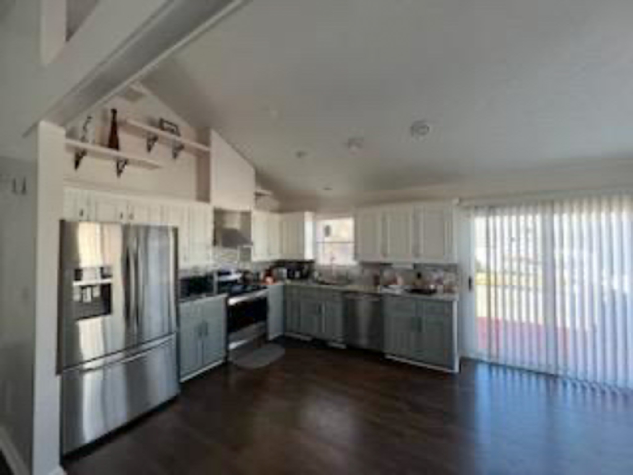A kitchen with stainless steel appliances, white cabinets, dark wood floors, and sliding glass doors letting in bright natural light inside the home of Sponsored Residential Provider Devonne Dixon in Lynchburg, Virginia.