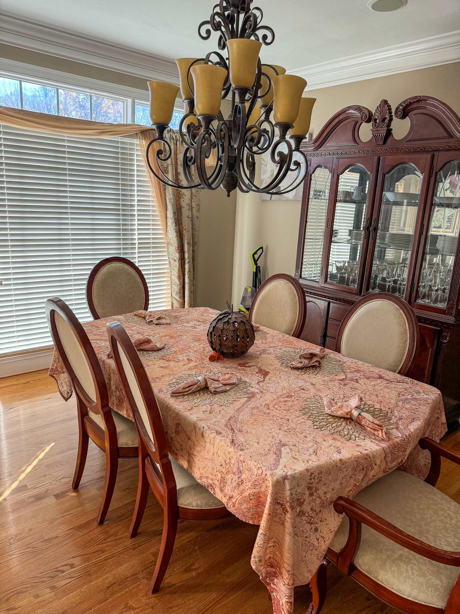 A dining room with tablecloth covered table, china cabinet, chandelier, and large window inside the home of Sponsored Residential Provider Sharon Jennings in Salem, Virginia.