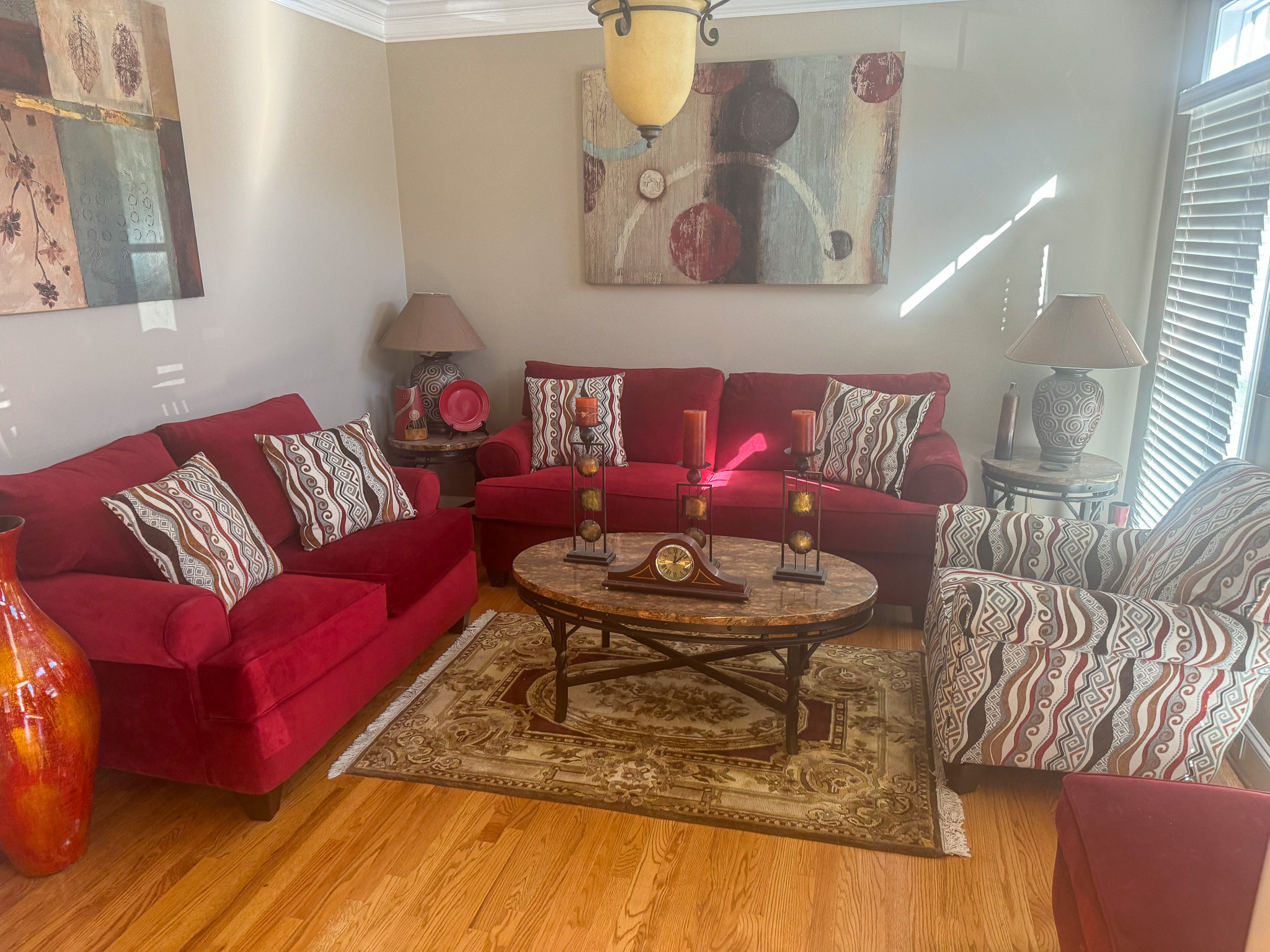 A living room with red sofas, patterned chairs, a round wooden coffee table, and abstract artwork on the walls inside the home of Sponsored Residential Provider Sharon Jennings in Salem, Virginia.