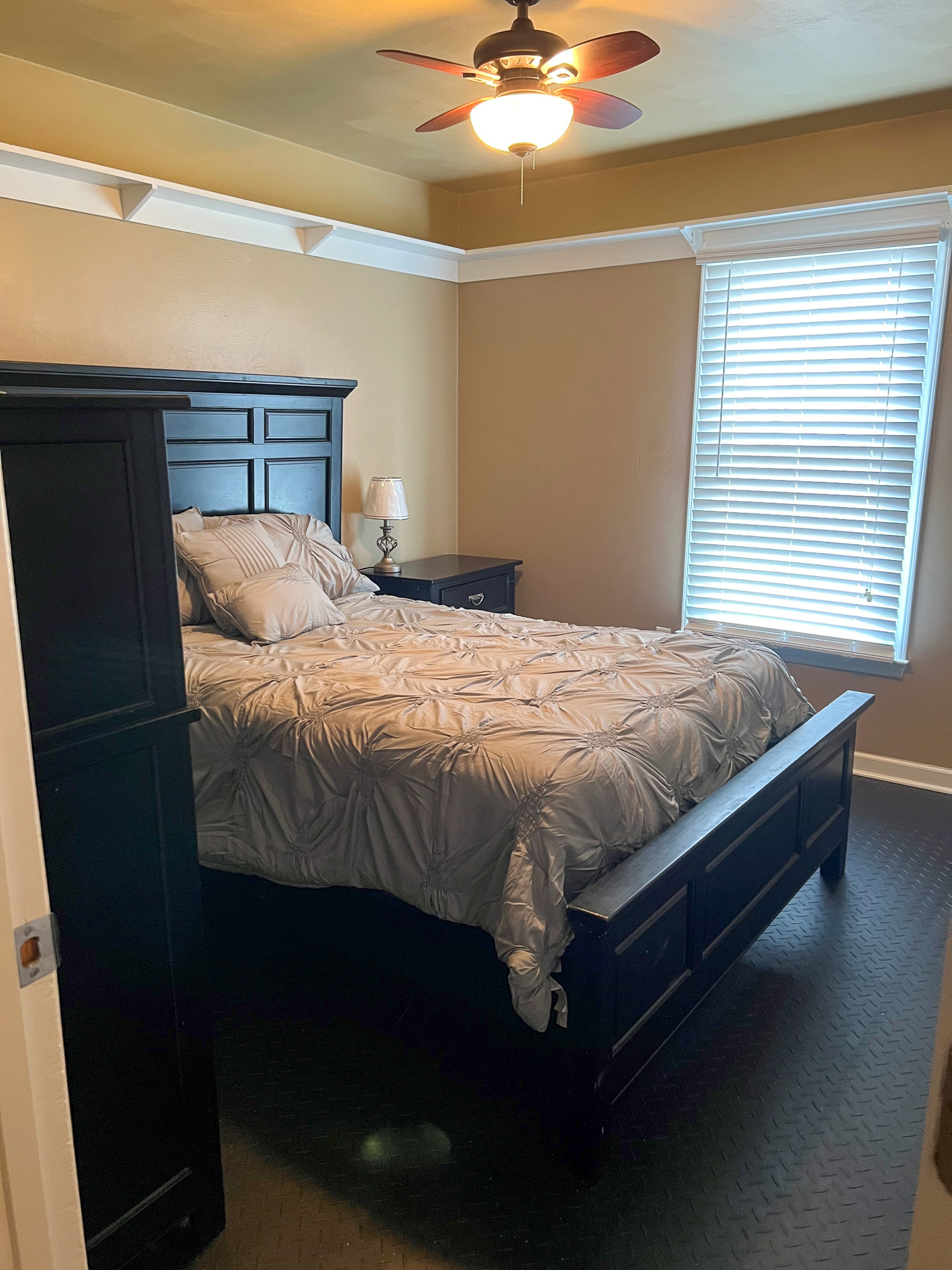 A bedroom with beige walls, dark wood furniture, a neatly made bed, and a ceiling fan with a light inside the home of Group Home Providers Anthony and Melissa Johnson in Daleville, Virginia.