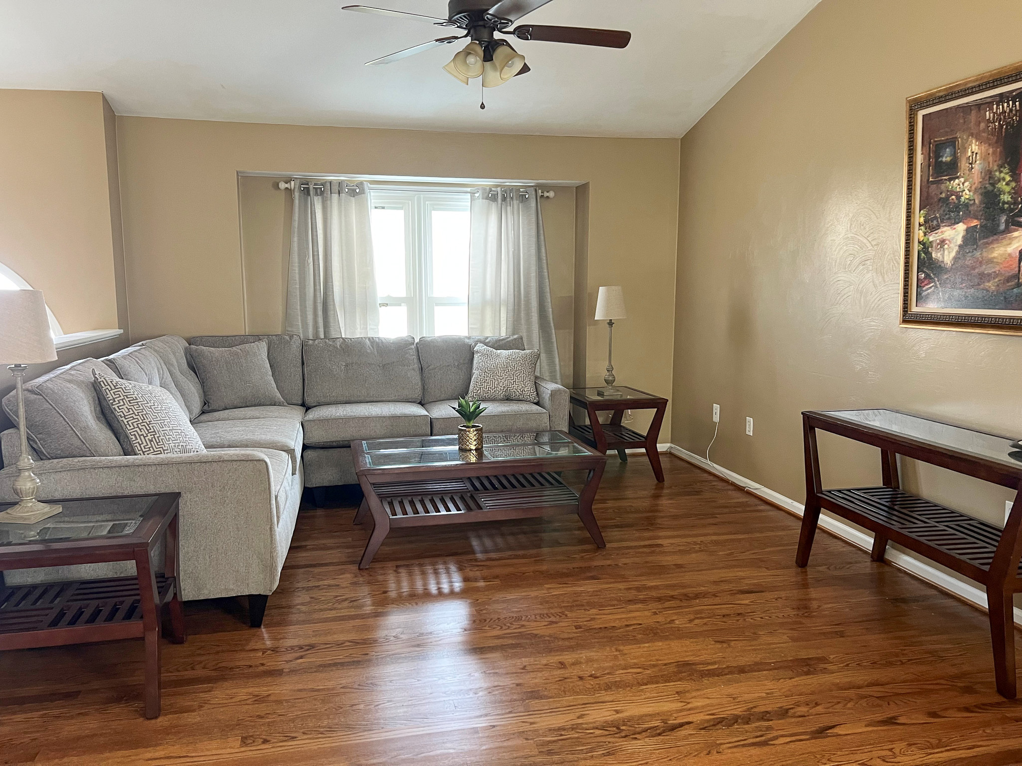 A living room with a light gray sectional sofa, glass-top tables, a ceiling fan, and hardwood floors inside the home of Group Home Providers Anthony and Melissa Johnson in Daleville, Virginia.