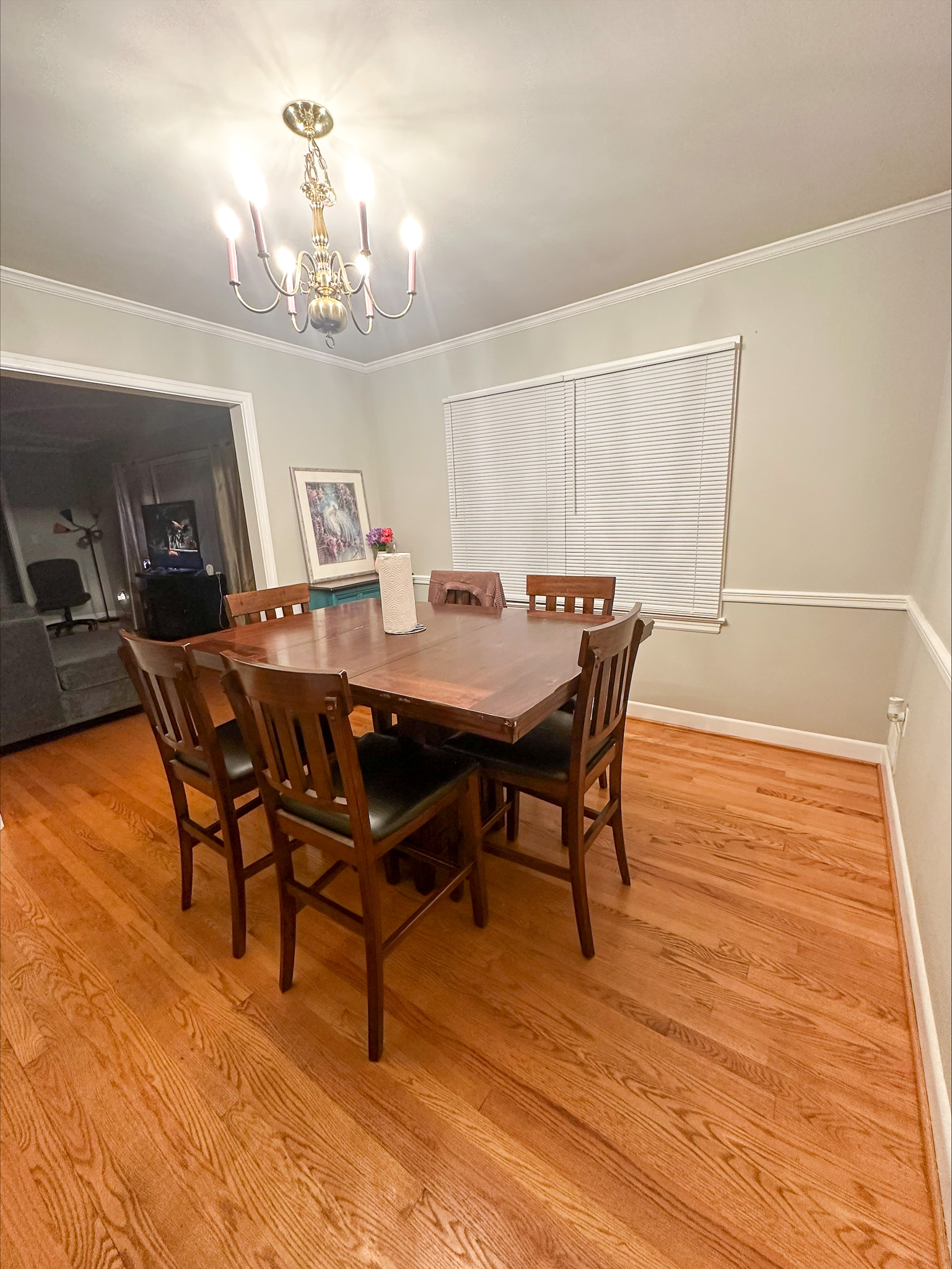 A dining room with a wooden table, matching chairs, hardwood floors, and a chandelier overhead inside the home of Group Home Provider Tina Langhorn in Roanoke, Virginia.