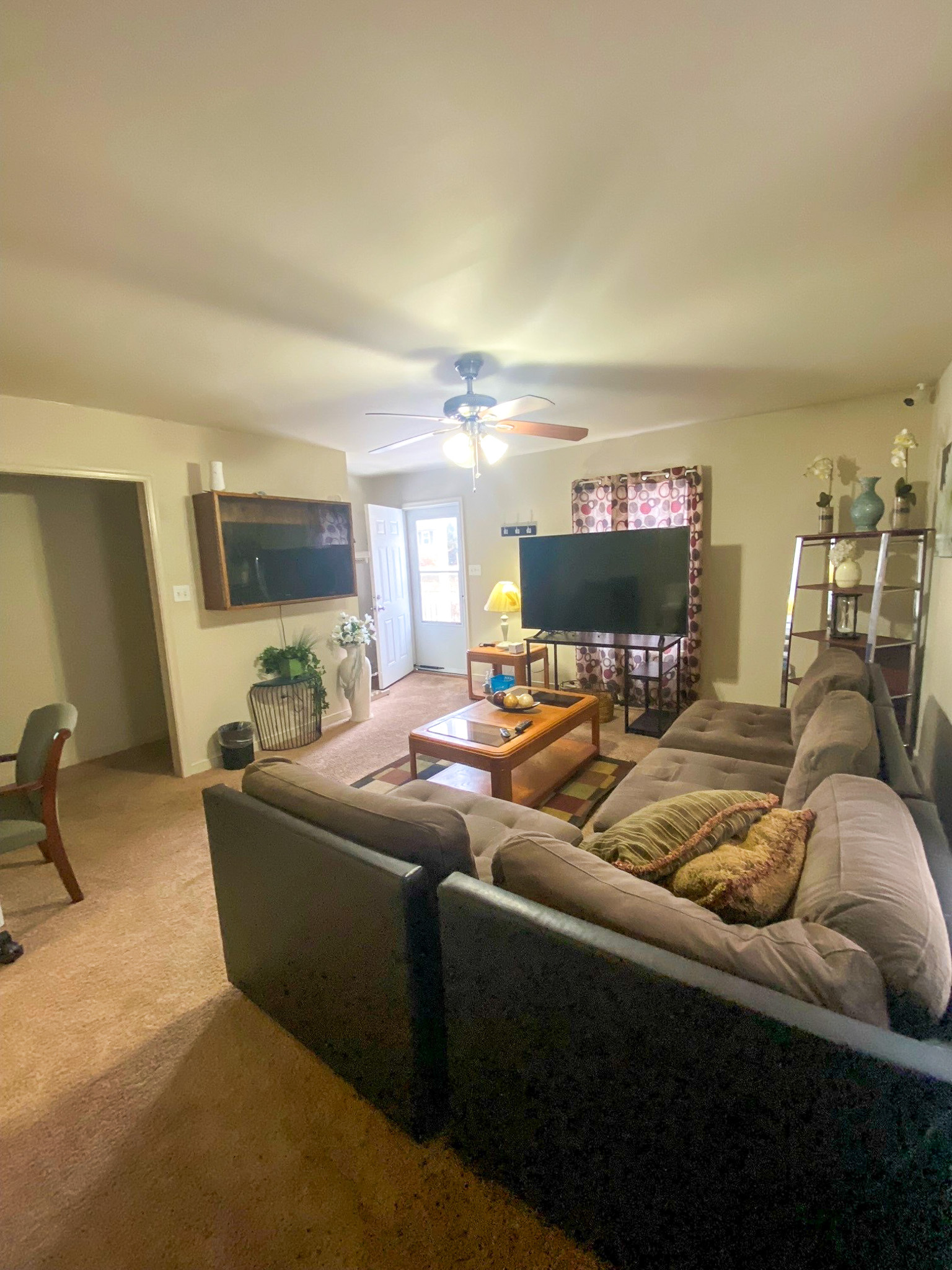 A living room with a large sectional sofa facing a TV, with a coffee table and shelving arranged around the seating area inside the home of Sponsored Residential Providers Xaiver Heath and David Williams in Richmond, Virginia.