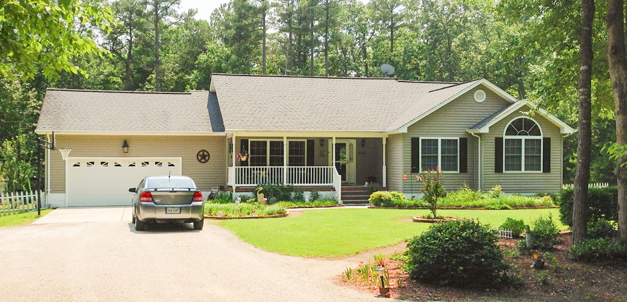 Single‑story tan house with a front porch, attached garage, landscaped yard, and a car parked in the driveway, surrounded by tall pine trees belonging to Sponsored Residential Provider Kellie Lynch in Gloucester, Virginia.