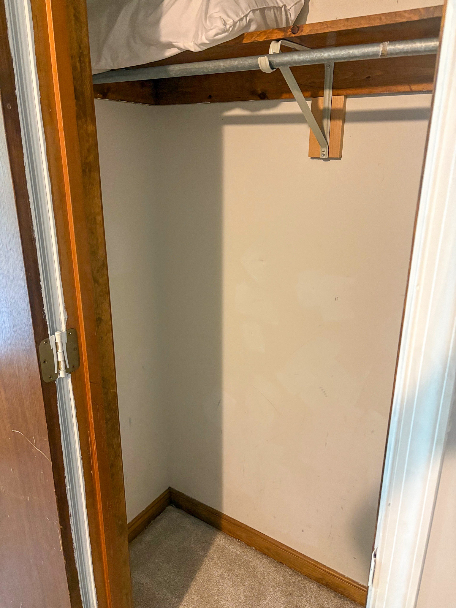 A small closet with a wooden rod and shelf is shown empty except for folded linens on the upper shelf inside the home of Group Home Provider Lelia Mabry in Midlothian, Virginia.