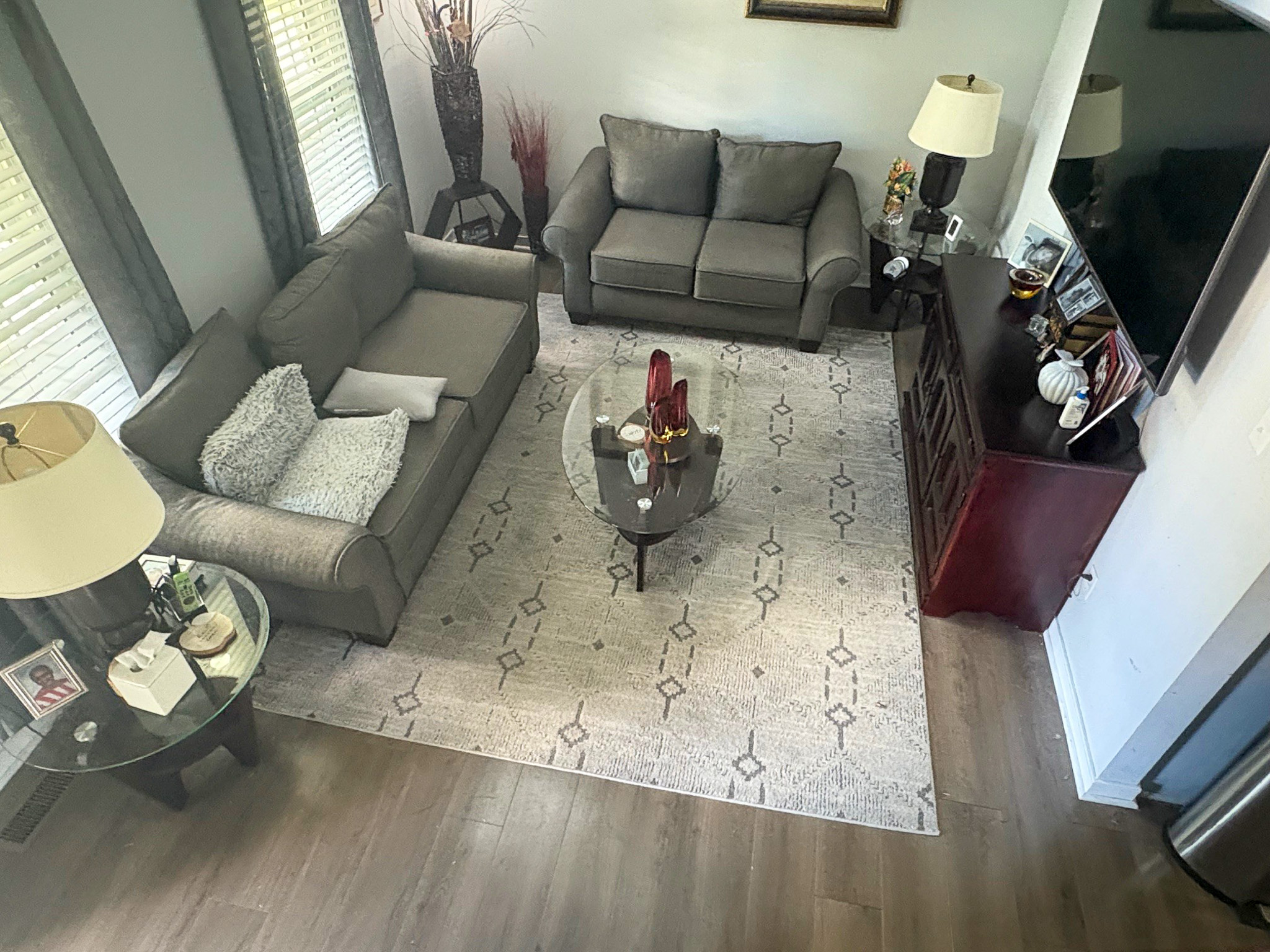 A living room is arranged with two gray sofas, a patterned rug, a glass coffee table, and a media console topped with decor inside the home of Group Home Provider Lelia Mabry in Midlothian, Virginia.